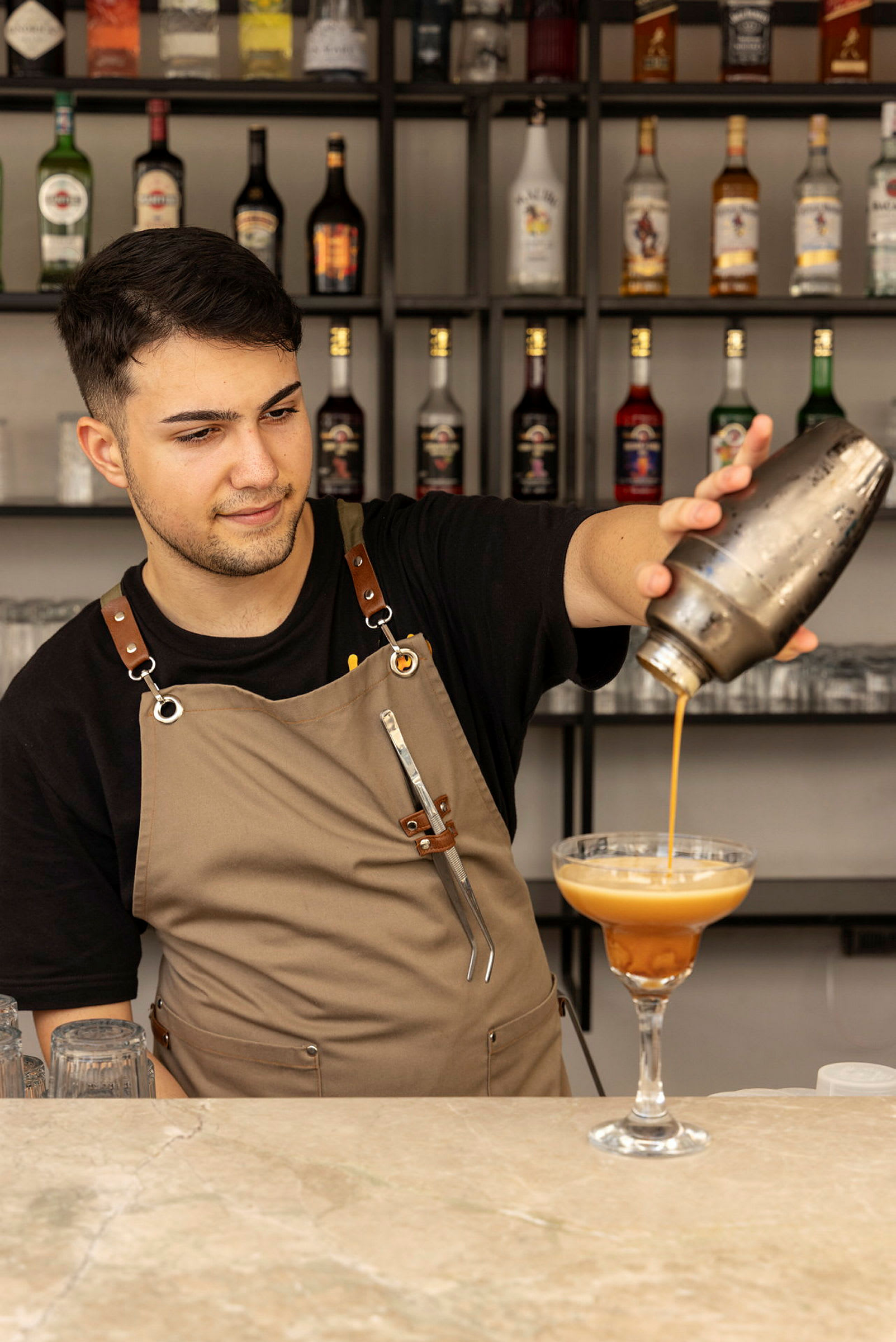 Baarimikko kaataa juomaa shakerista cocktail-lasiin. (Tekoälyn luoma teksti)