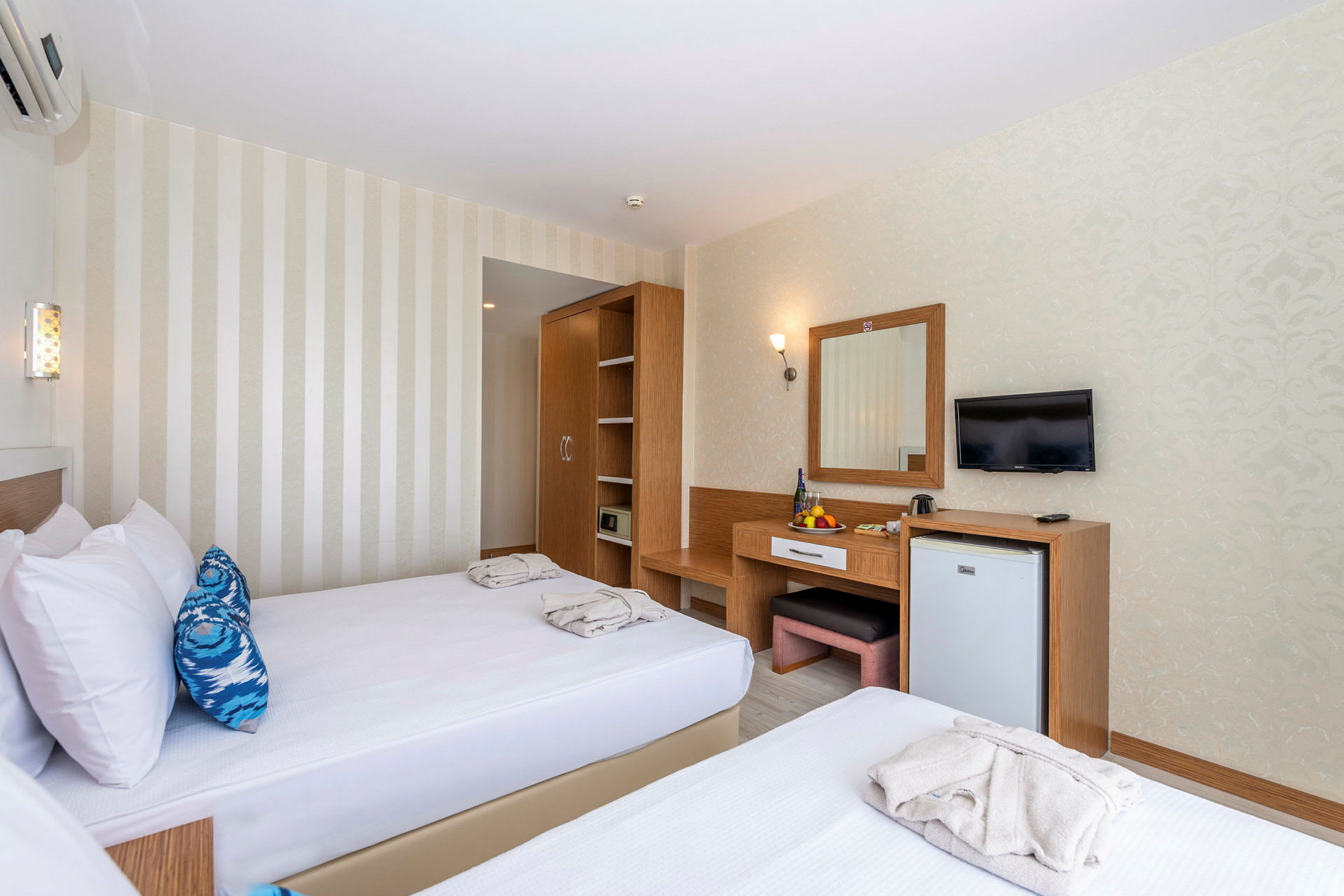 Hotellihuone, jossa kaksi erillistä vuodetta, vaatekaappi, työpöytä peilillä ja seinälle kiinnitetty TV. (Tekoälyn luoma teksti)