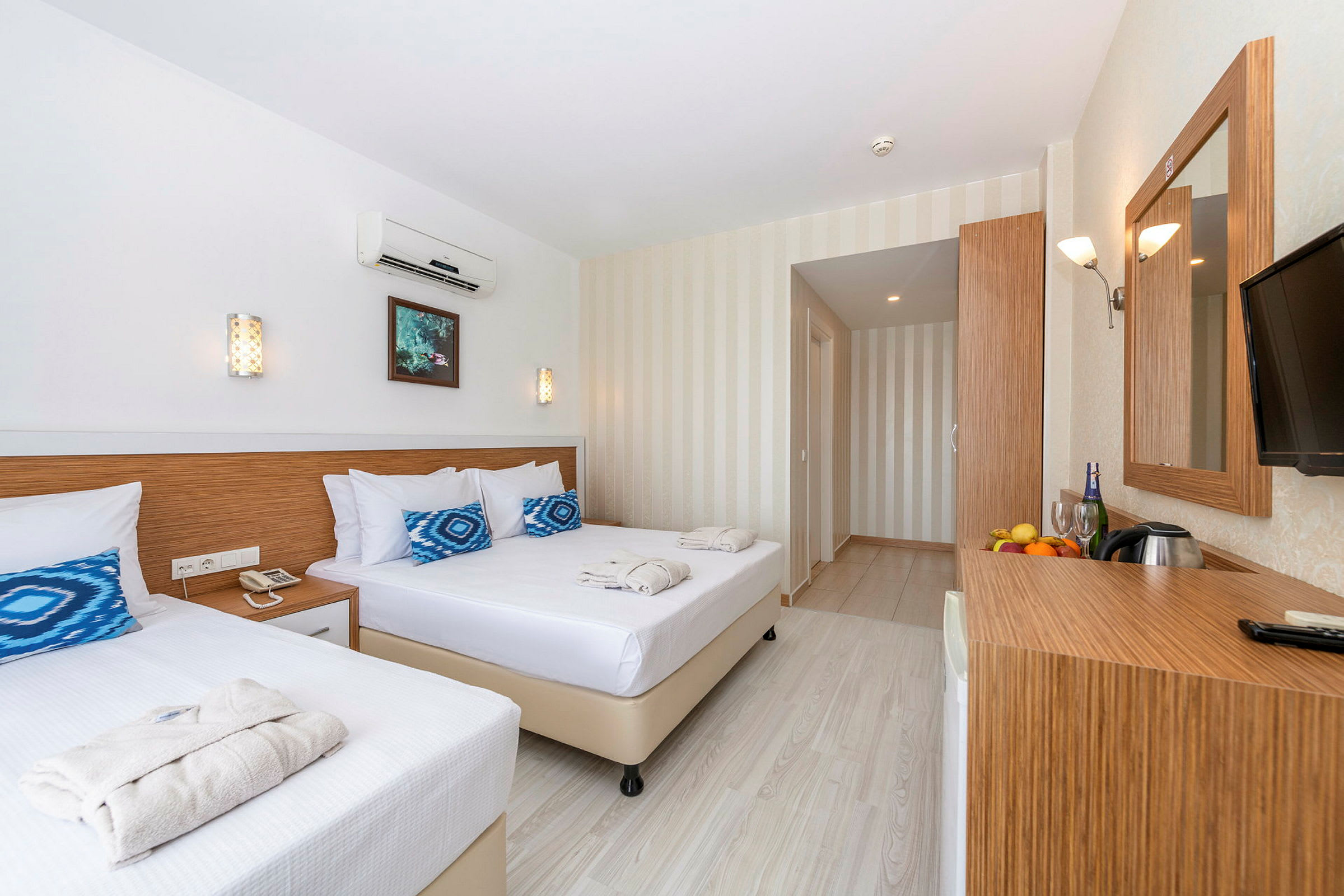 Valoisa ja moderni hotellihuone, jossa on kaksi sänkyä, peili ja kirjoituspöytä hedelmineen ja juomineen. (Tekoälyn luoma teksti)