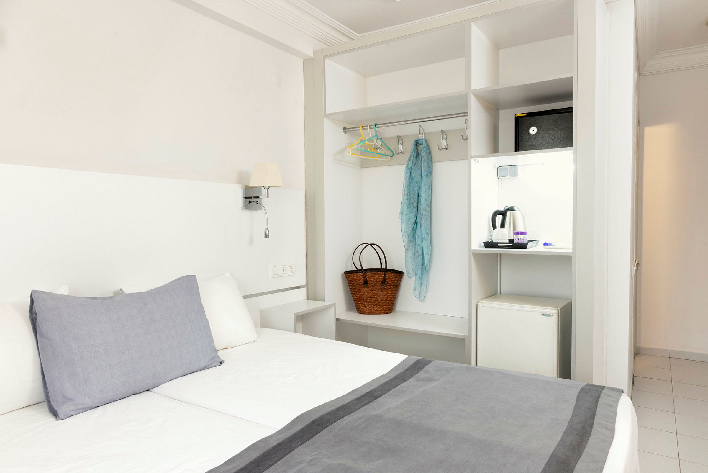 Hotellihuone, jossa sänky, vaatekaappi ja pieni jääkaappi. (Tekoälyn luoma teksti)