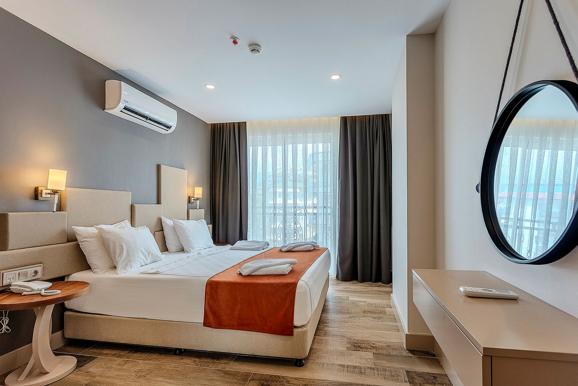 Hotellihuone, jossa on parivuode, yöpöytä, koristeellinen peili seinällä ja ikkunat verhoilla. (Tekoälyn luoma teksti)