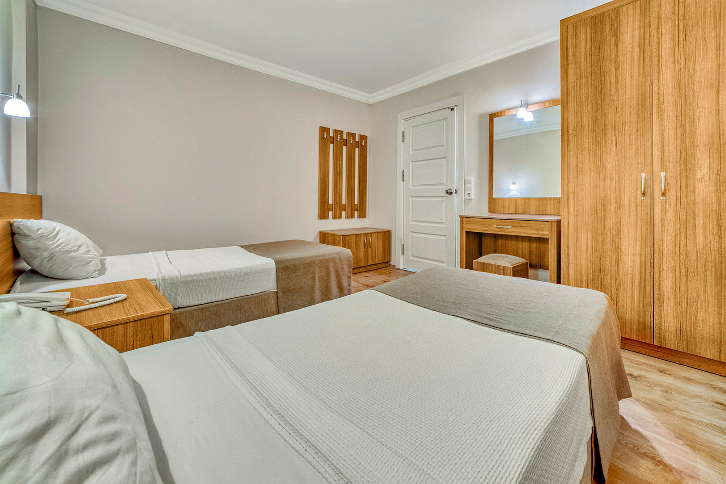Hotellihuoneen sisustus, jossa kaksi erillistä vuodetta, puukaappeja ja meikkipöytä. (Tekoälyn luoma teksti)