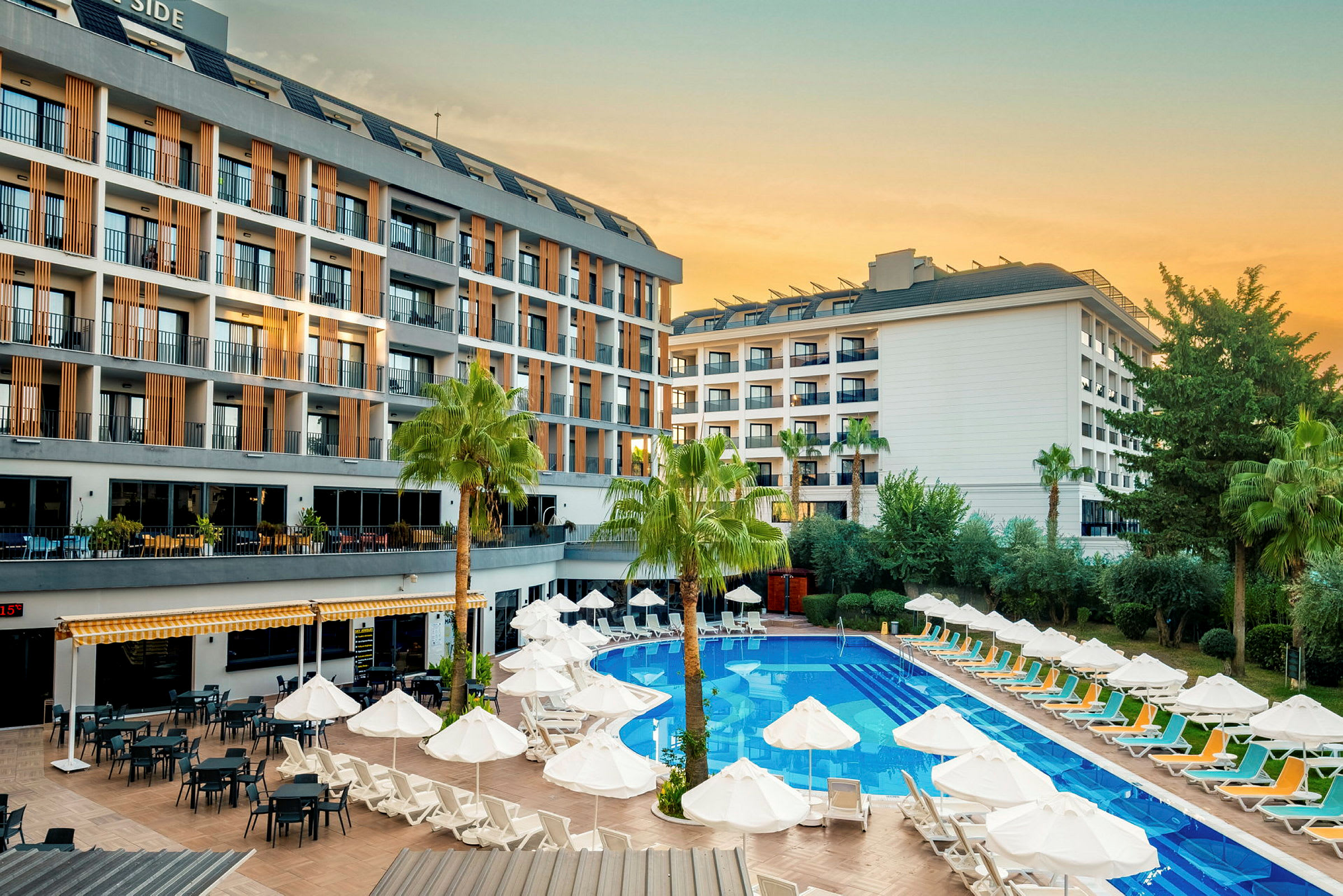 Hotellirakennus, jossa allasalue, aurinkotuoleja ja varjoja. (Tekoälyn luoma teksti)