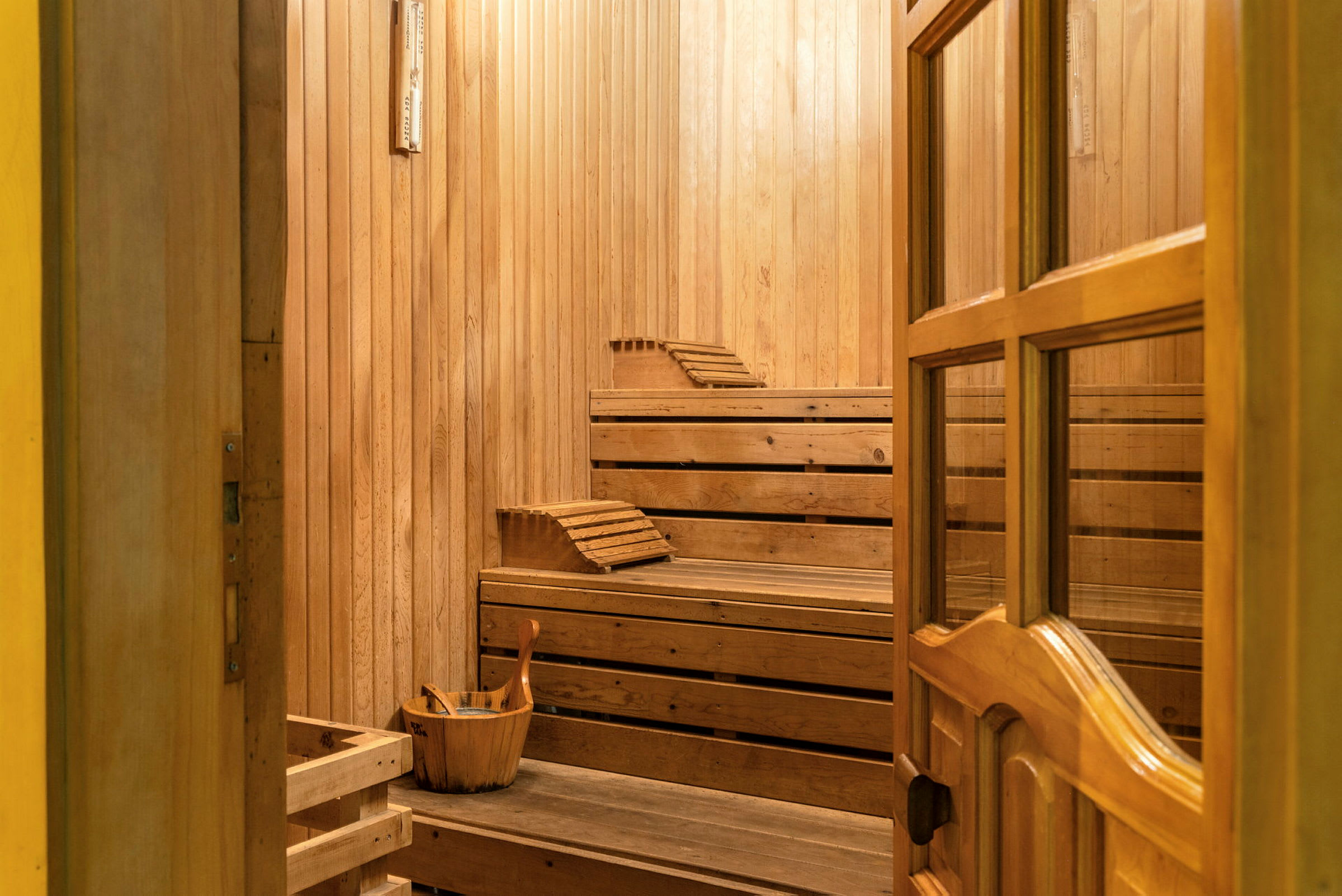 Sauna, jossa on puuseinät, penkit ja ämpäri kauhalla. (Tekoälyn luoma teksti)