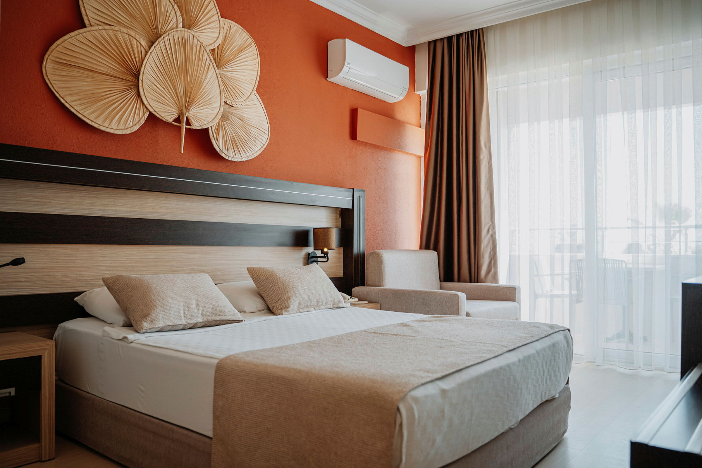 Hotellihuone, jossa oranssi seinä, parivuode kahdella tyynyllä sekä koriste-esineitä sängyn yläpuolella. (Tekoälyn luoma teksti)