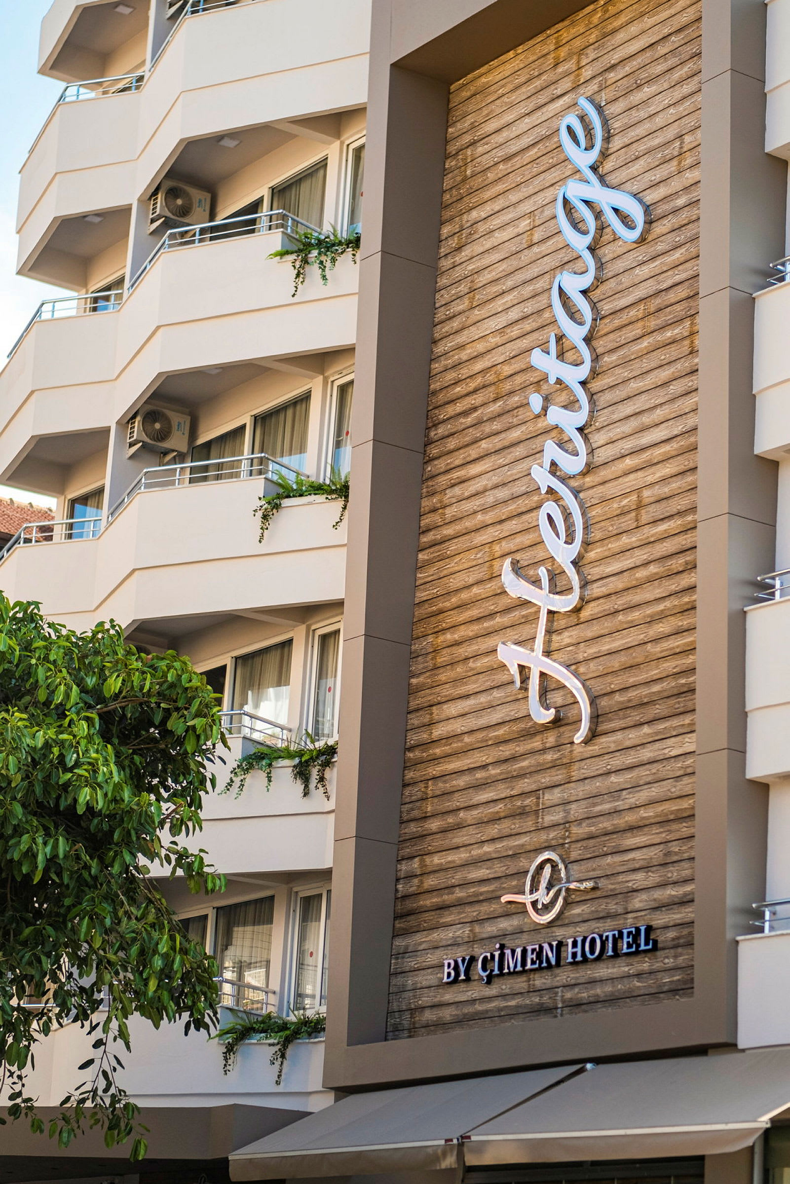 Moderni hotelli parvekkeilla ja kyltti tekstillä 'Heritage by Çimen Hotel'. (Tekoälyn luoma teksti)