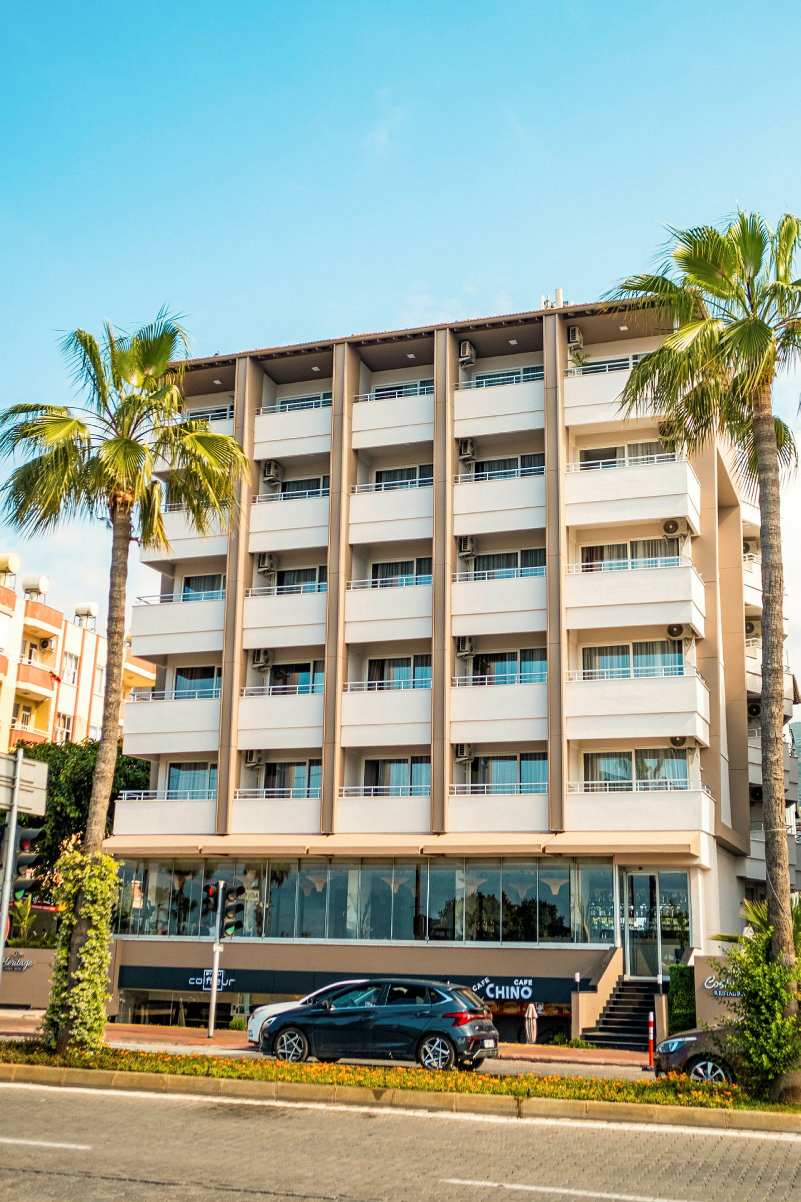 Kuva monikerroksisesta hotellista, palmuista ja autosta etualalla. (Tekoälyn luoma teksti)
