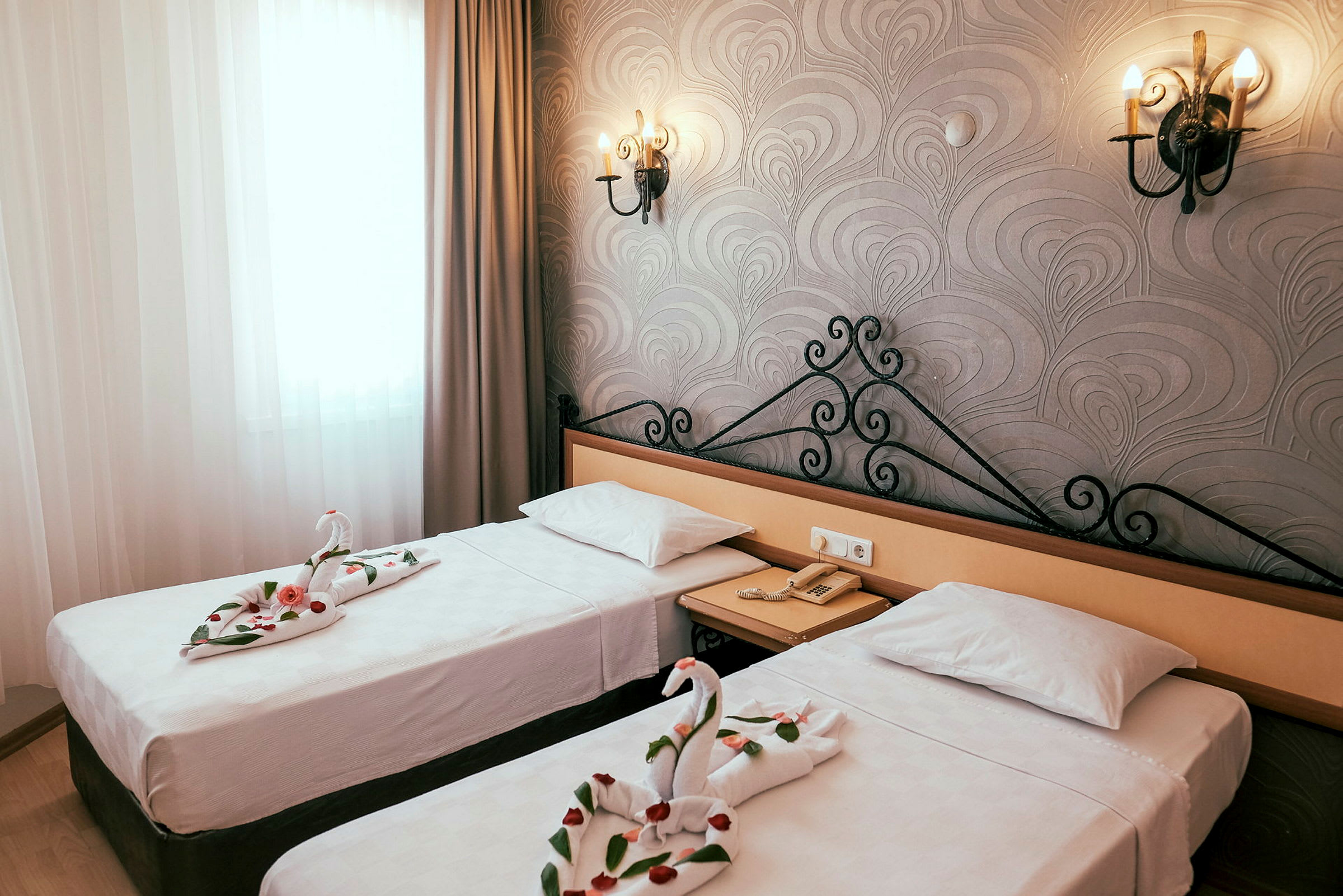 Kuva hotellihuoneesta, jossa on kaksi erillistä sänkyä. Sängyillä olevat pyyhkeet on taiteltu joutsenen muotoon ja koristeltu ruusun terälehdillä. (Tekoälyn luoma teksti)