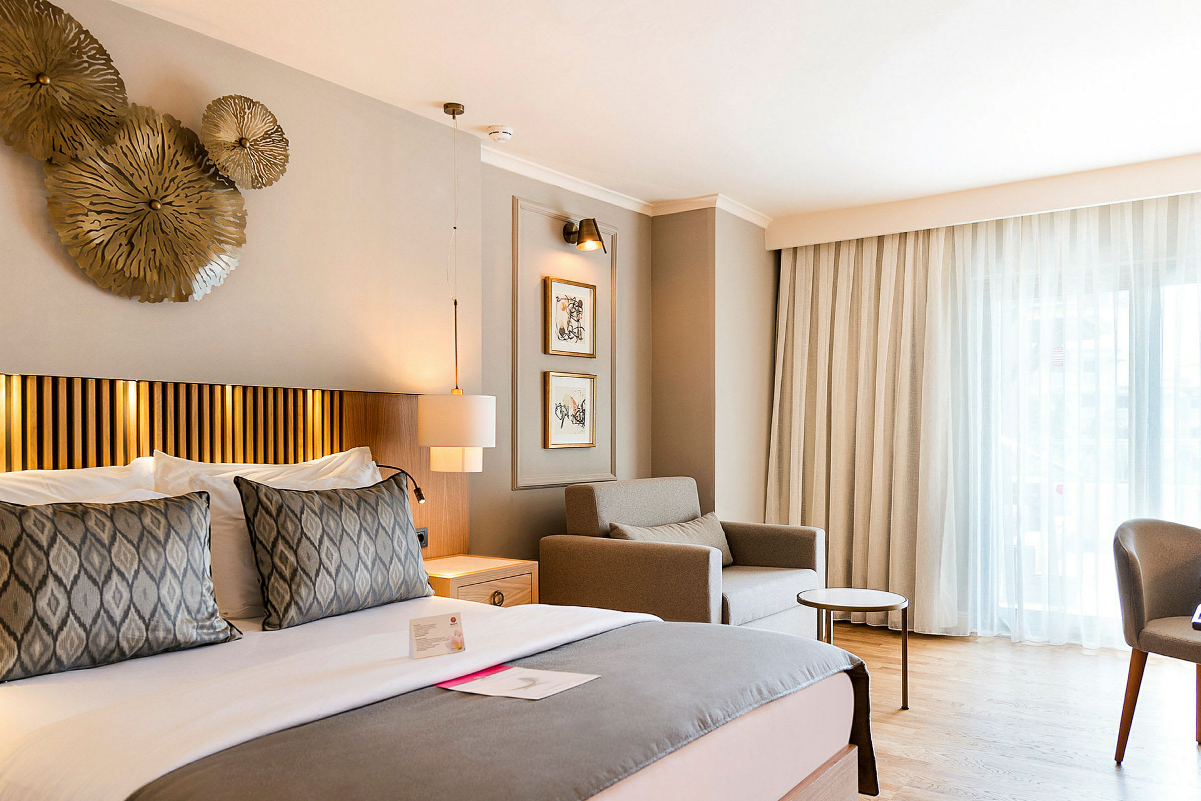 Hotellihuone, jossa suuri sänky, nojatuoli ja pöytä ikkunan äärellä. (Tekoälyn luoma teksti)
