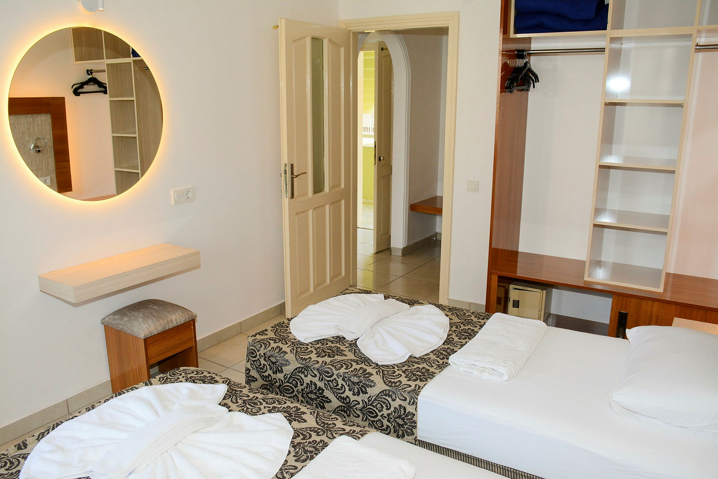 Hotellihuone, jossa on kaksi yhden hengen vuodetta, vaatekaappi ja pyöreä peili seinällä. (Tekoälyn luoma teksti)