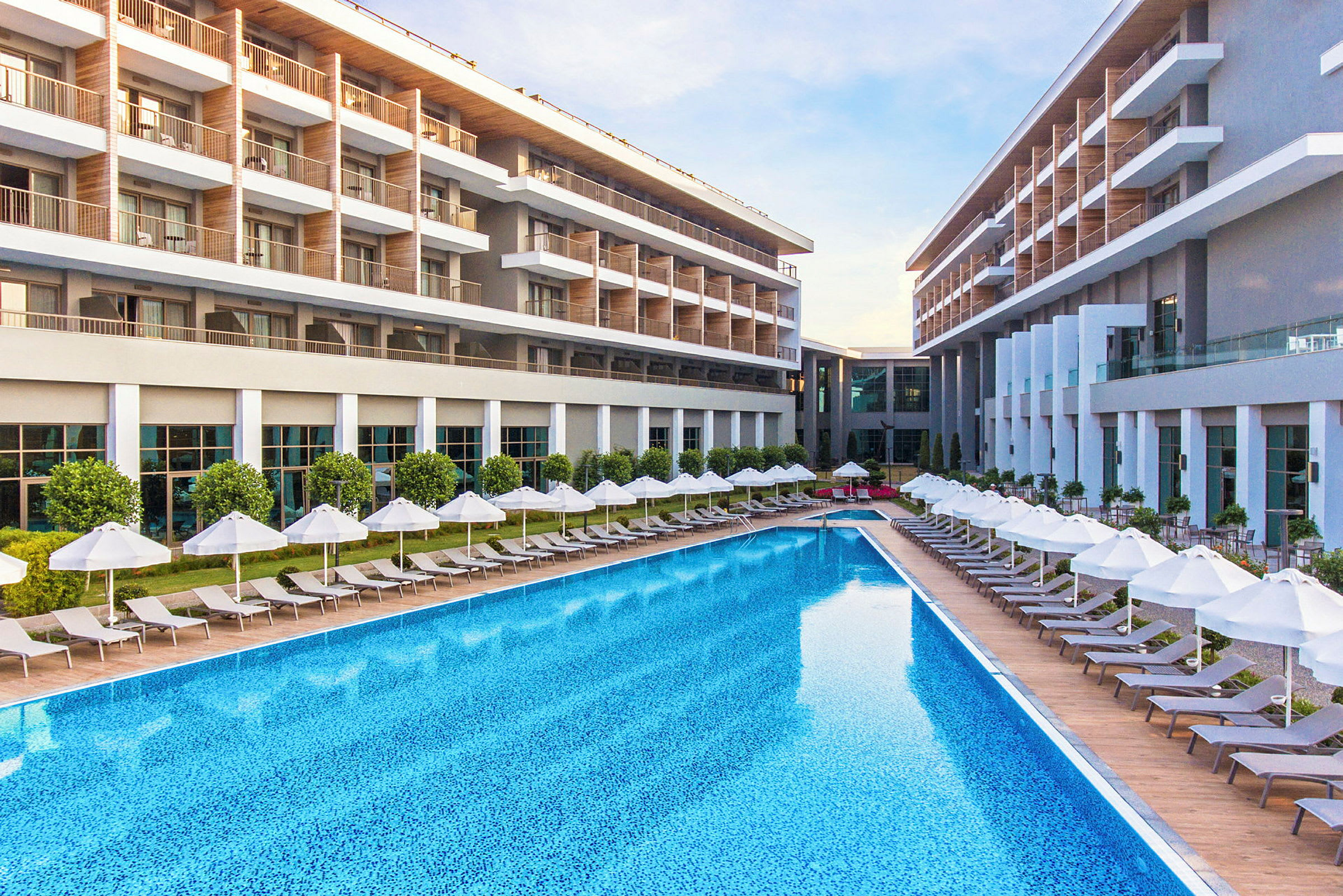 Moderni hotellirakennus, jossa suuri uima-allas ja aurinkotuoleja varjoineen. (Tekoälyn luoma teksti)