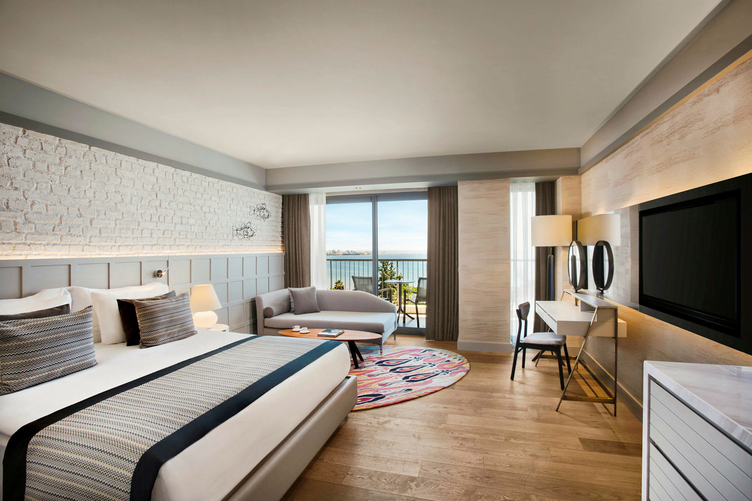 Hotellihuone, jossa suuri sänky, istuinalue ja parveke merinäköalalla. (Tekoälyn luoma teksti)