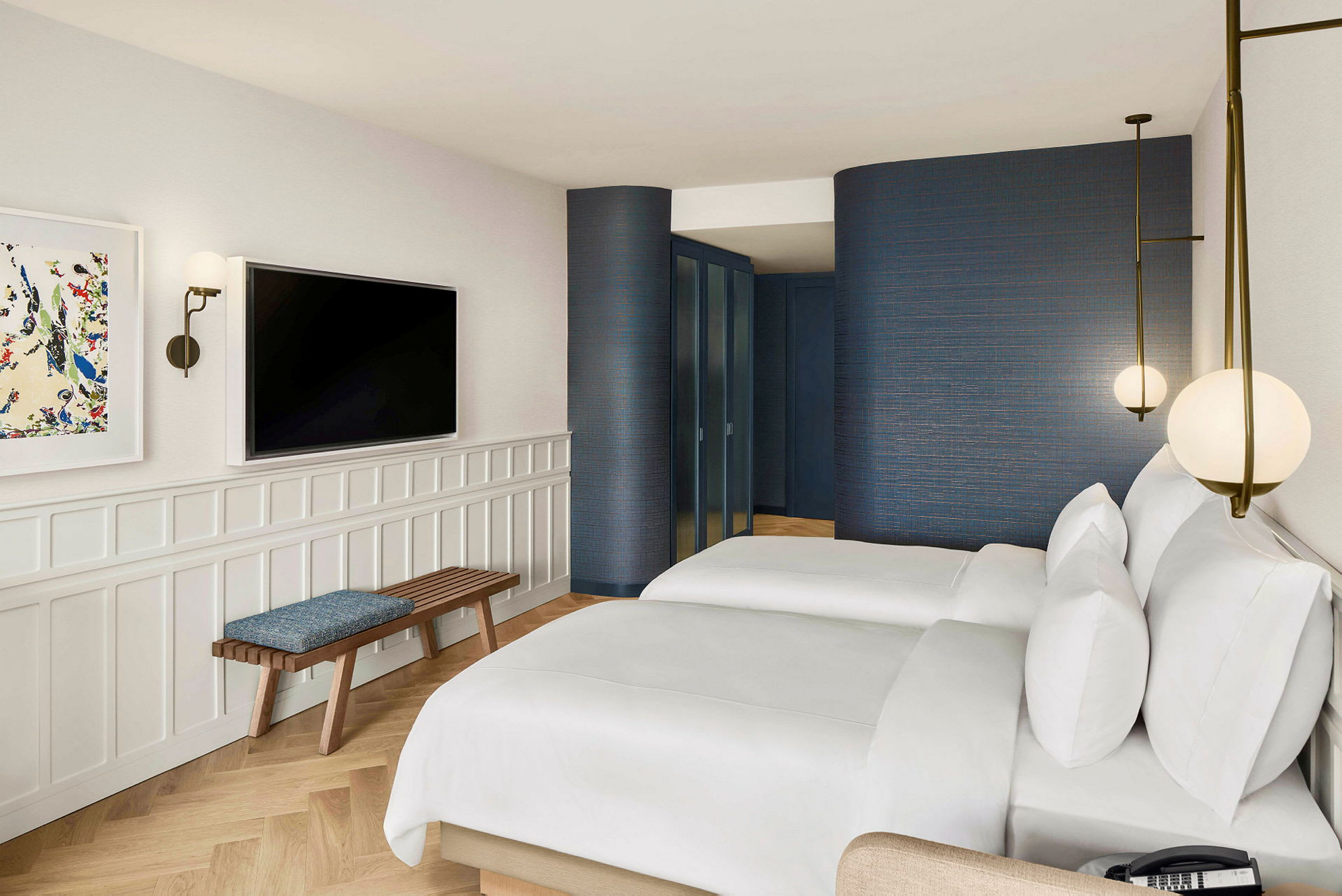 Hotellihuone, jossa kaksi sänkyä, seinä televisiolla ja penkki. (Tekoälyn luoma teksti)