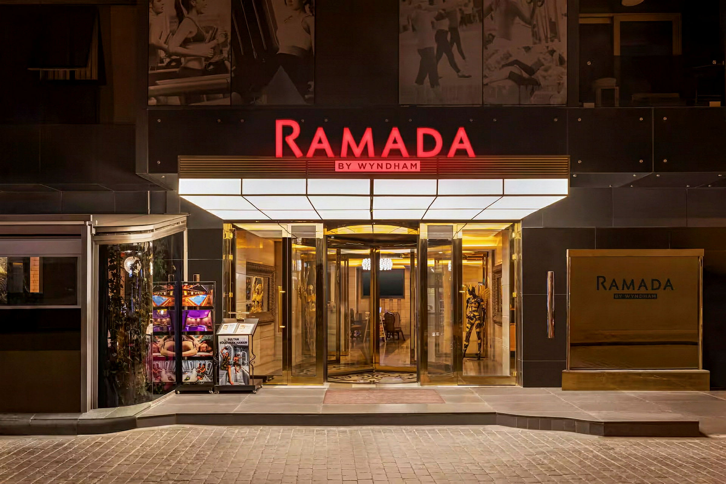 Ramada by Wyndham -hotelliketjun pääsisäänkäynti pyörivällä ovella ja kylteillä. (Tekoälyn luoma teksti)