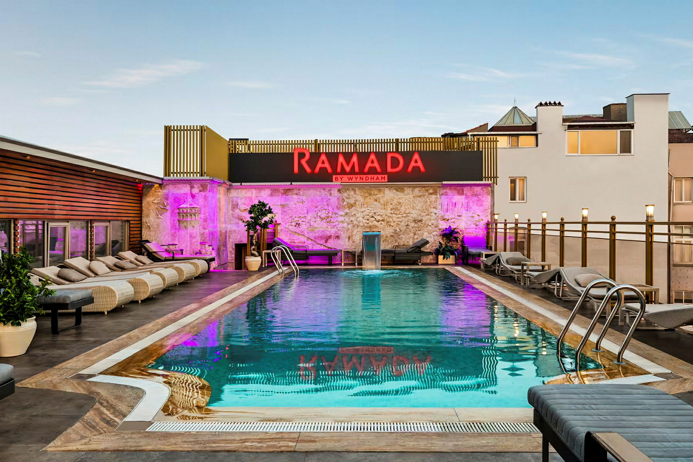Kuva ulkouima-altaasta, ympärillä aurinkotuoleja ja kyltti tekstillä Ramada by Wyndham. (Tekoälyn luoma teksti)