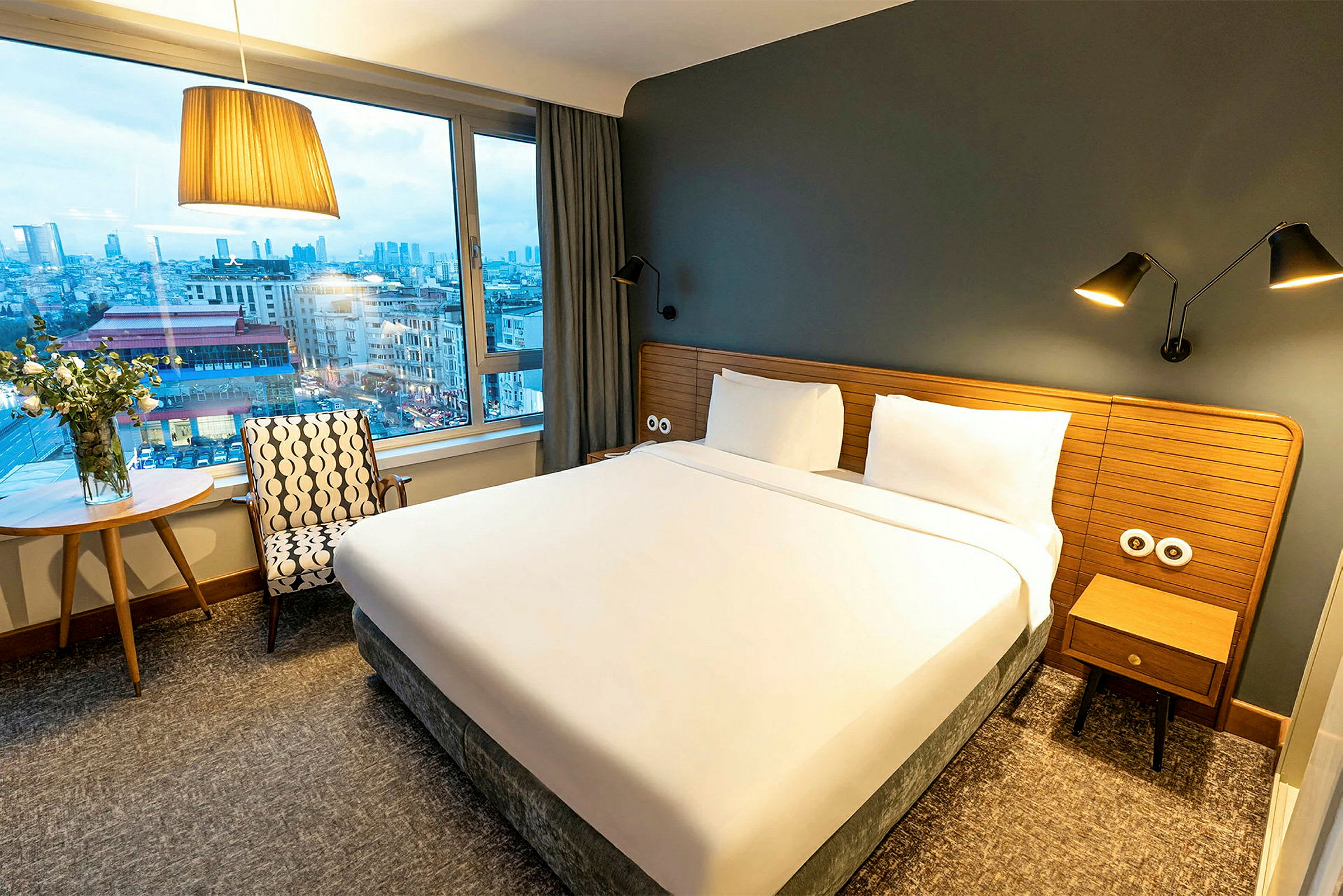 Hotellihuone, jossa suuri sänky, ikkuna ja näkymä kaupunkiin. (Tekoälyn luoma teksti)