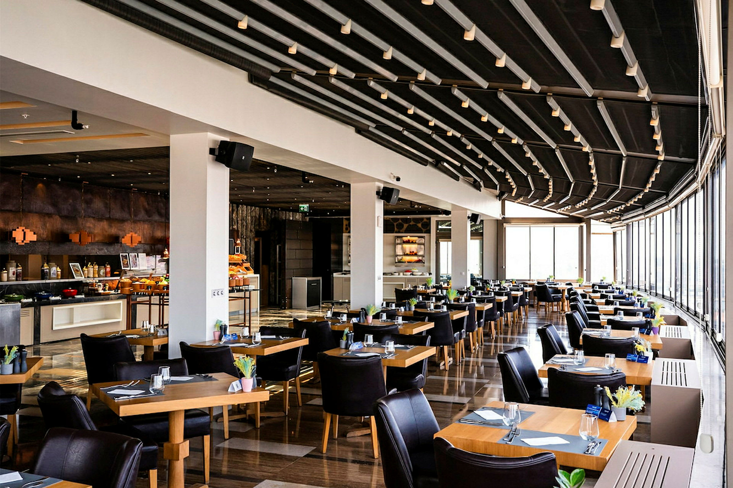 Ravintola, jossa on nykyaikaisesti sisustettuja pöytiä ja tuoleja, iso ikkunapinta, joka päästää valoa sisään. (Tekoälyn luoma teksti)