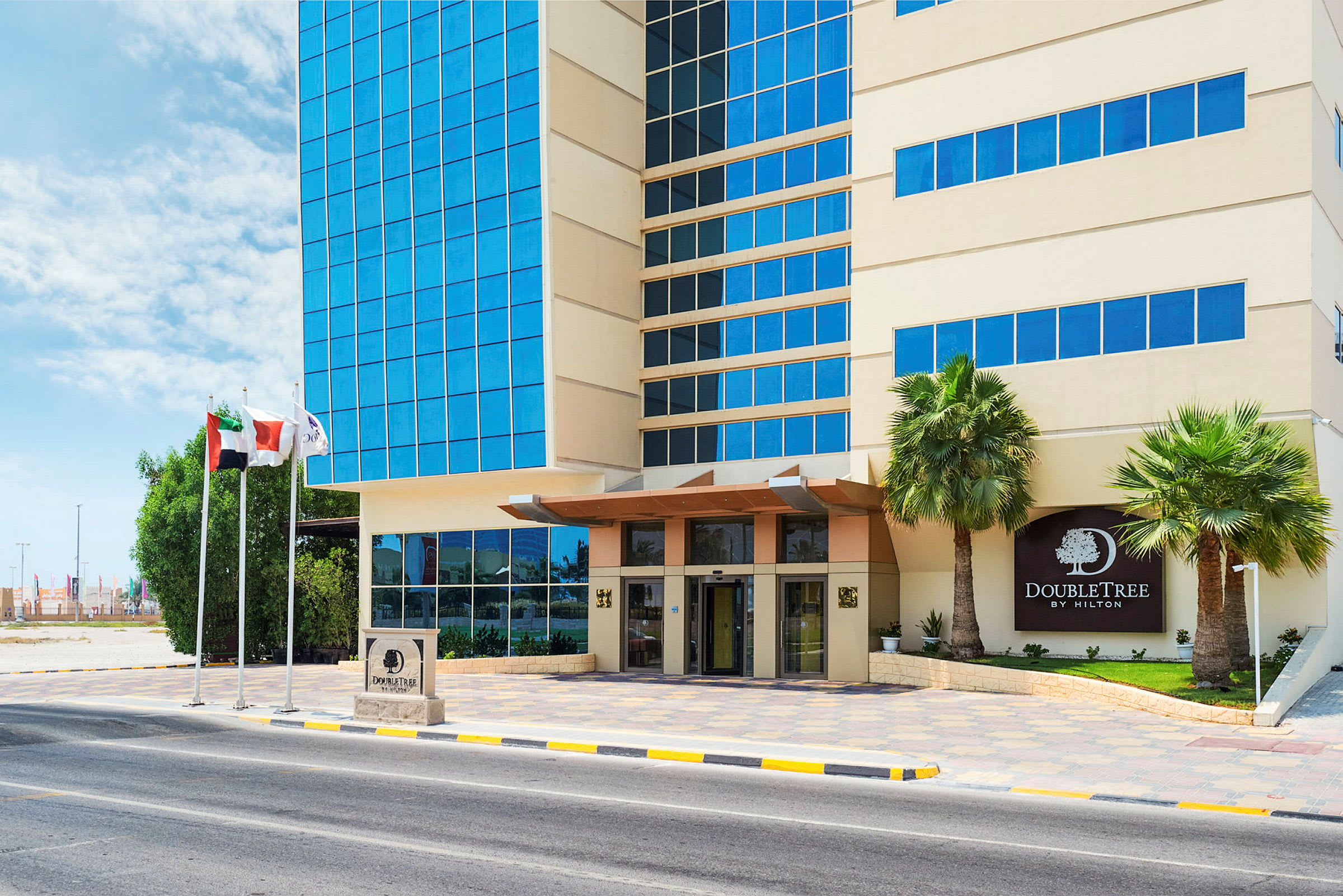 DoubleTree-hotellin julkisivu, sisäänkäynti, lasiseinä ja palmuja vieressä. (Tekoälyn luoma teksti)