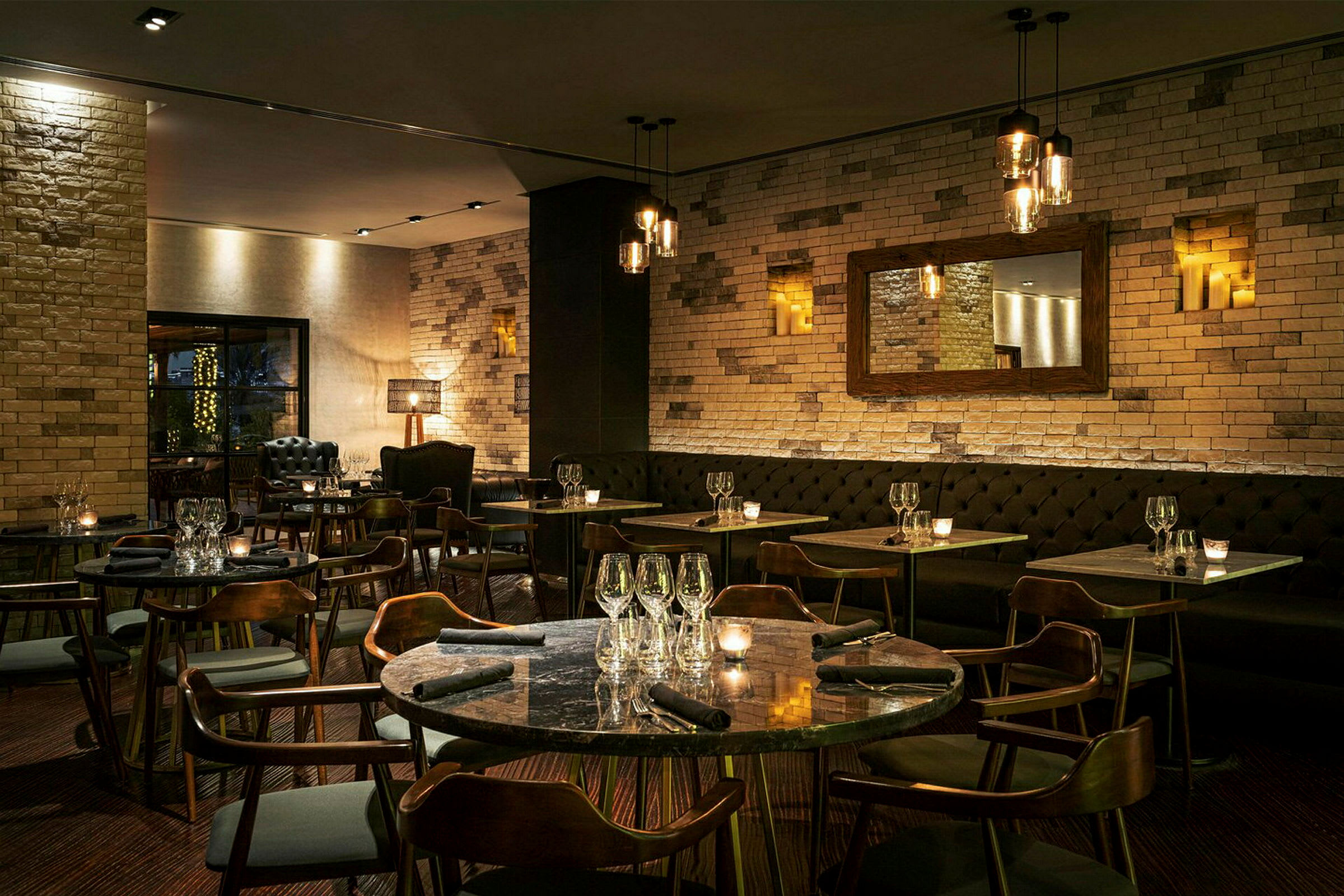 Tyylikäs ravintola, jossa on tiiliseinät, tummat kalusteet ja valaistus, luo viihtyisän tunnelman. (Tekoälyn luoma teksti)