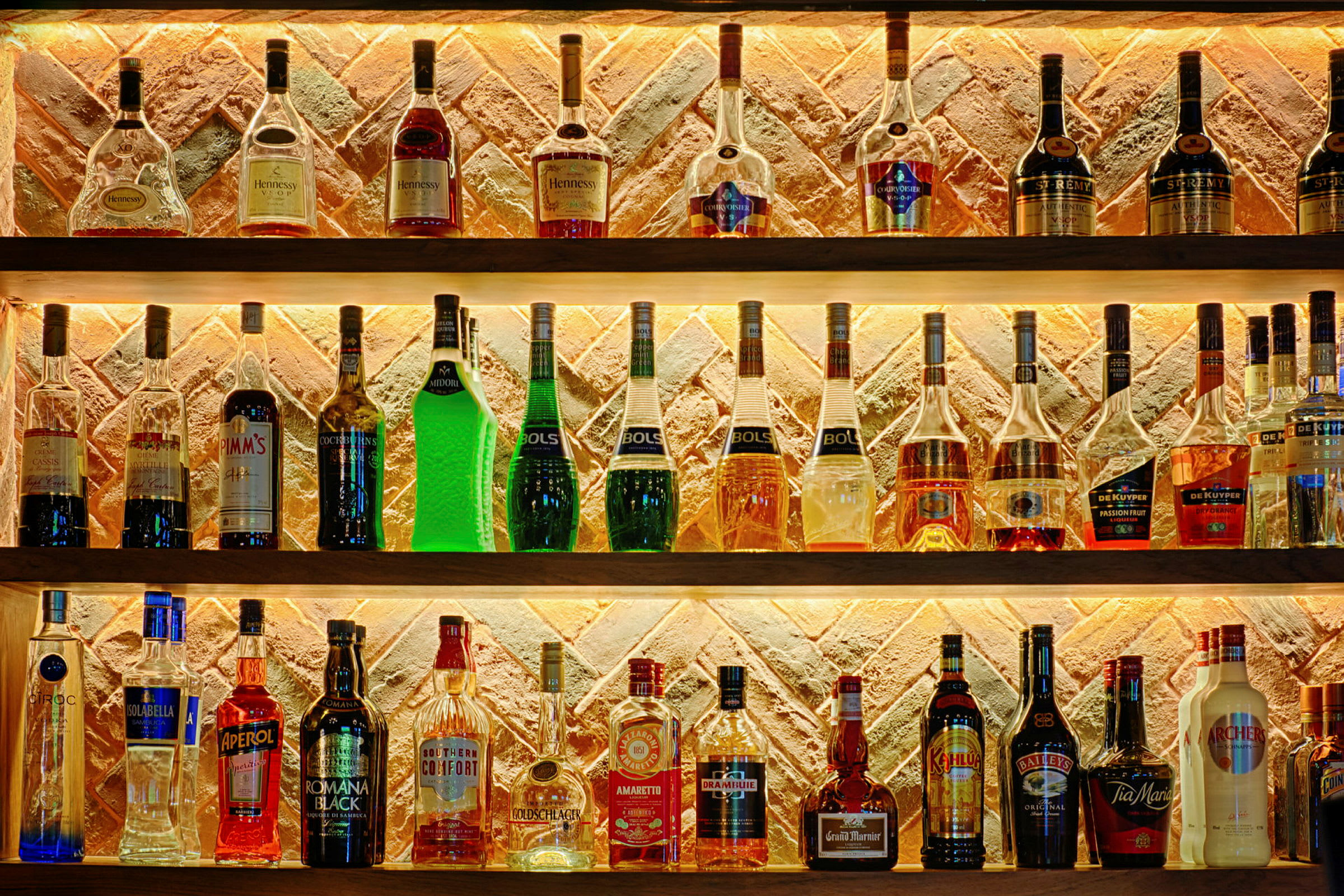 Useita hyllyjä, jotka on täynnä erilaisia alkoholipullotyyppejä tiiliseinän edessä. (Tekoälyn luoma teksti)