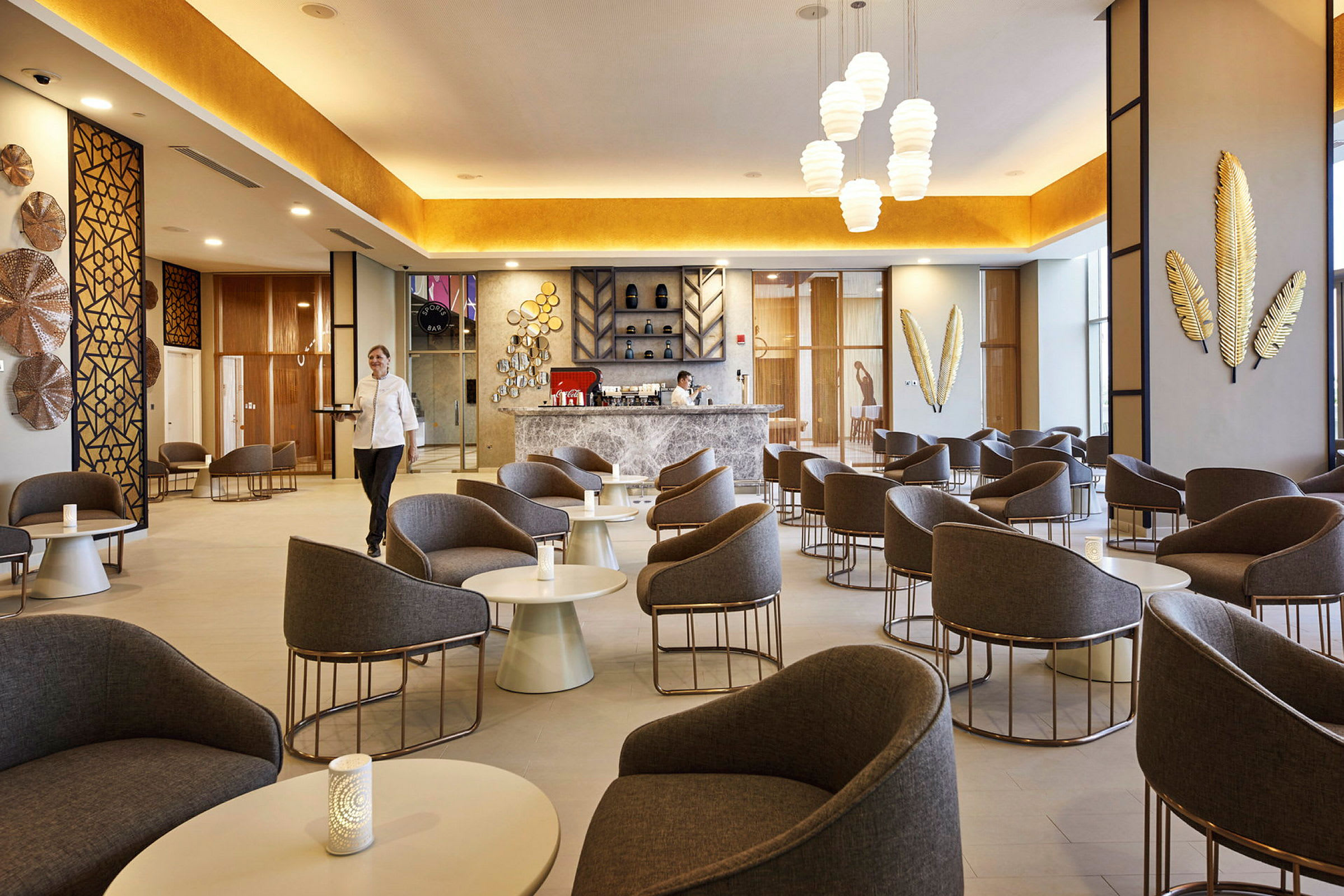 Moderni kahvila/lounge, jossa mukavat nojatuolit ja pöydät, koristeellisia seinäyksityiskohtia ja kutsuva baaritiski. (Tekoälyn luoma teksti)