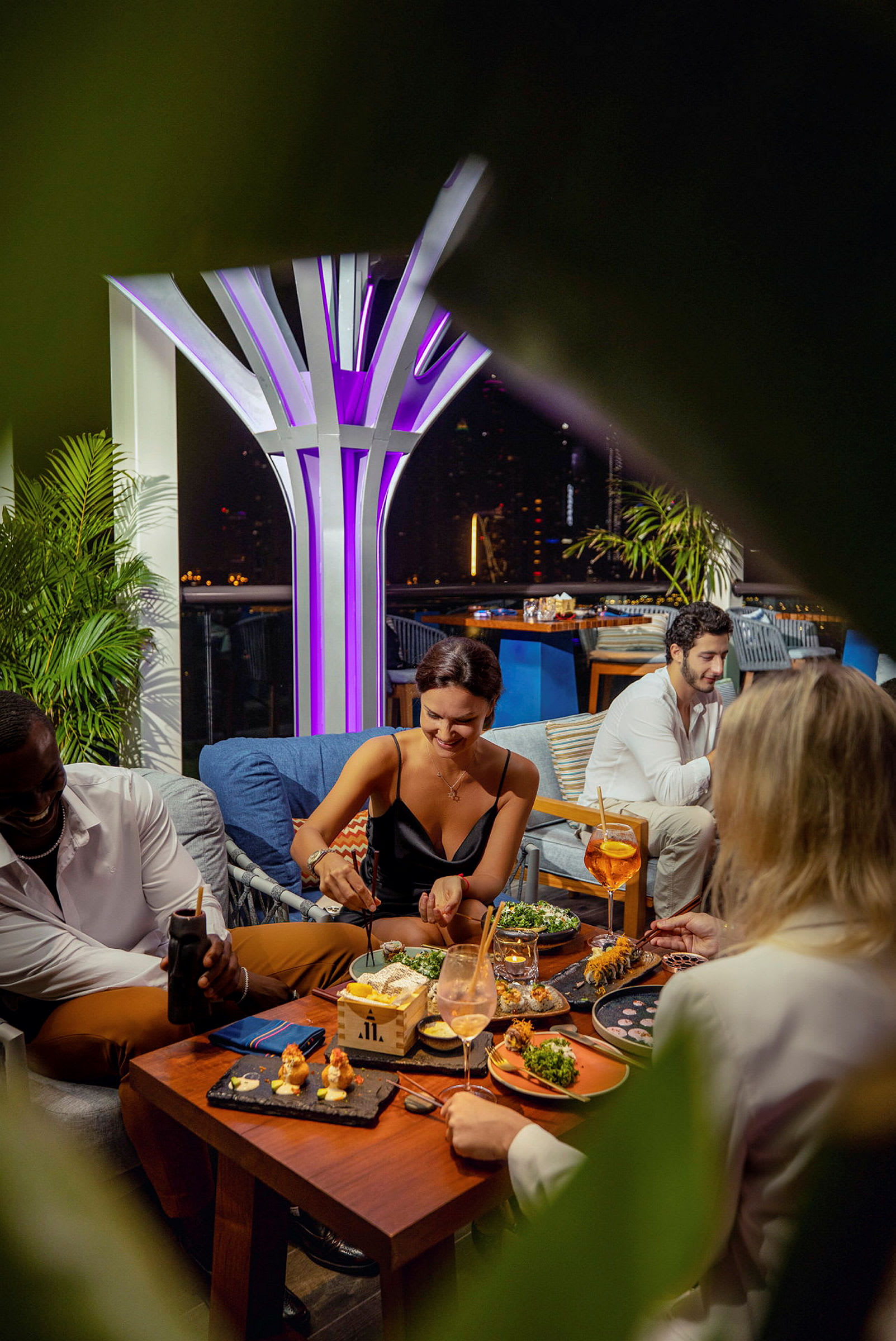 Ruokailukohtaus, jossa ihmiset syövät pöydän ääressä, ympäröitynä tyylikkäällä ympäristöllä, jossa on kirkas koristevalaistus. (Tekoälyn luoma teksti)