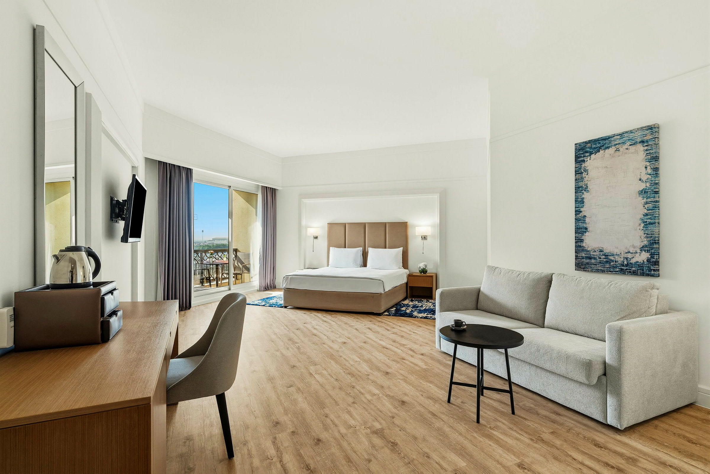 Hotellihuone, jossa on parivuode, sohva ja työpöytä, sekä parveke näköalalla. (Tekoälyn luoma teksti)