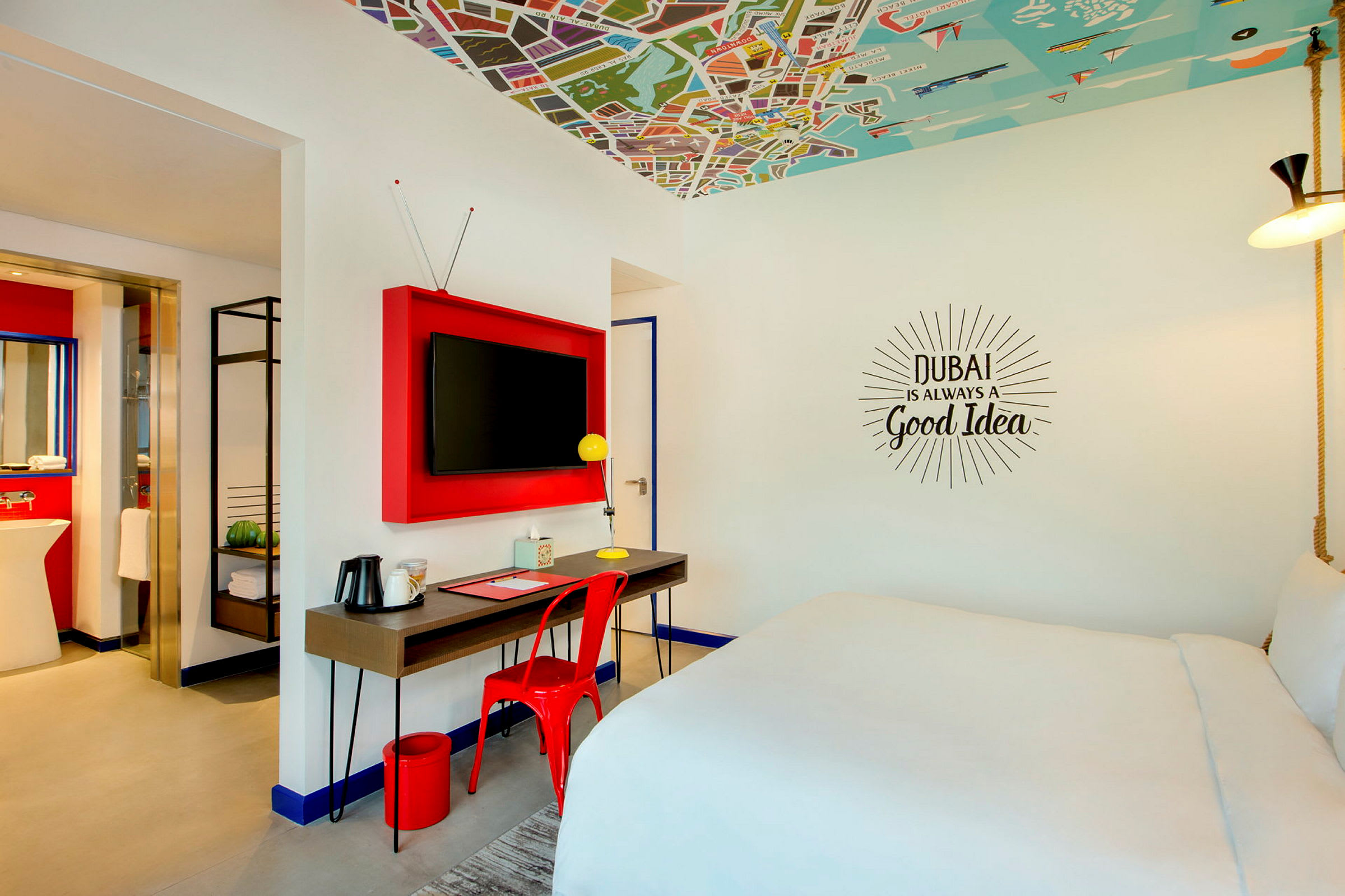 Modernisti sisustettu hotellihuone, jossa on iso sänky, kirjoituspöytä tuoleineen ja televisio seinällä. (Tekoälyn luoma teksti)