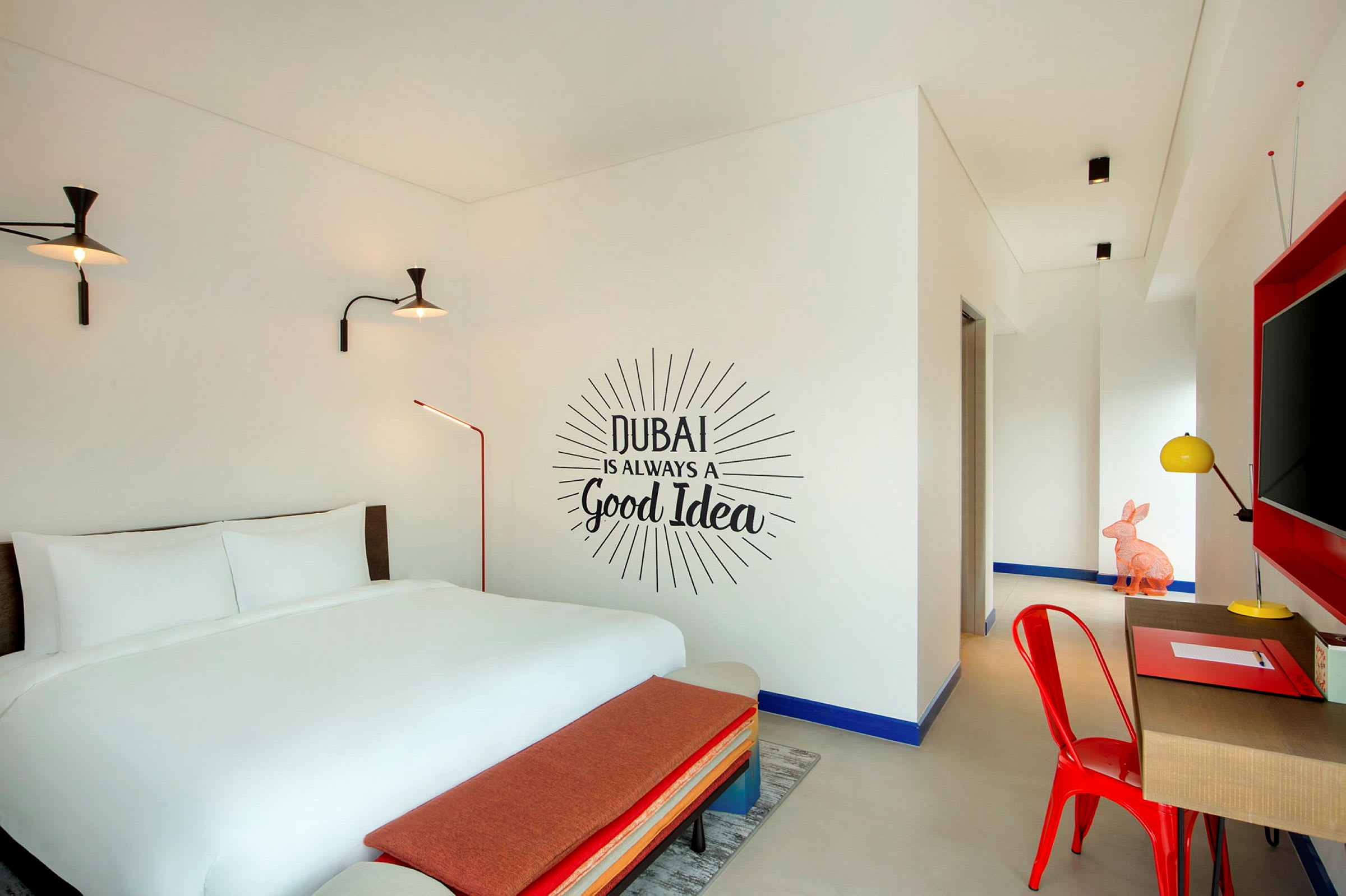 Hotellihuone, jossa on parivuode, seinäteksti "Dubai is always a good idea" ja nykyaikainen sisustus. (Tekoälyn luoma teksti)