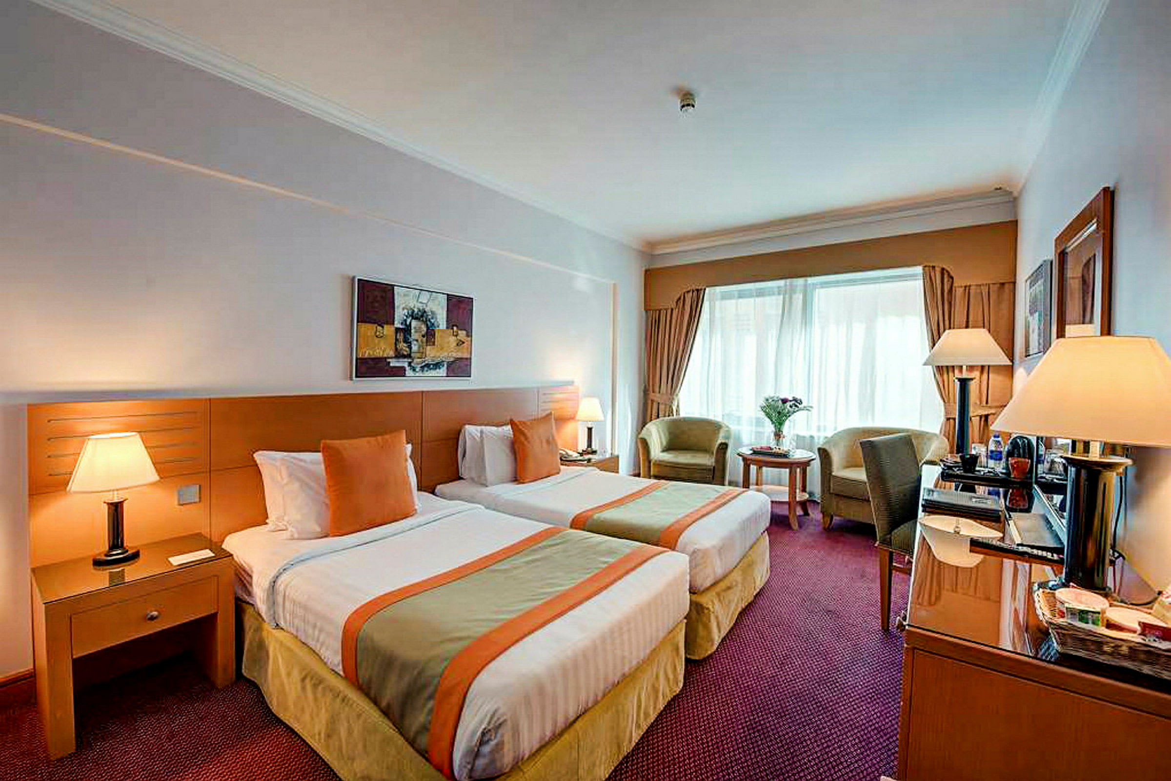 Hotellihuone, jossa on kaksi yhden hengen vuodetta, pöytä, tuolit ja lamput. (Tekoälyn luoma teksti)