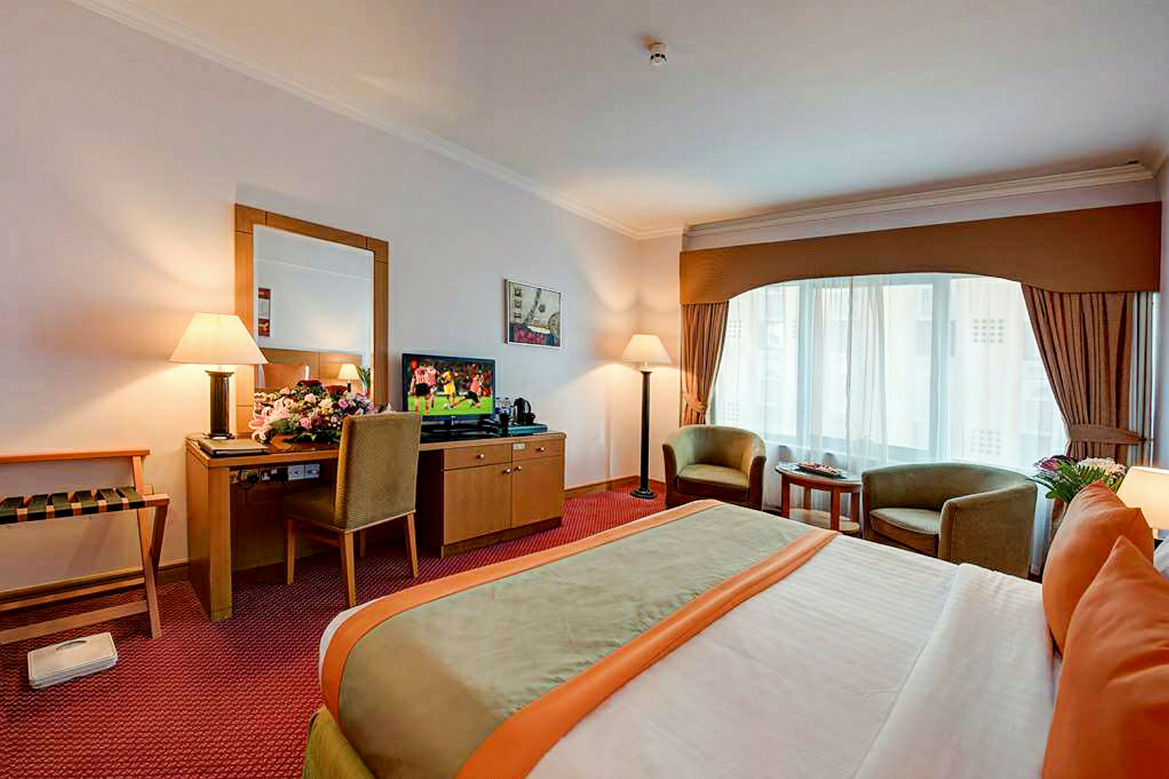 Hotellihuone, jossa on parisänky, kaksi nojatuolia suuren ikkunan edessä sekä televisio laatikoston päällä kirjoituspöydän vieressä. (Tekoälyn luoma teksti)