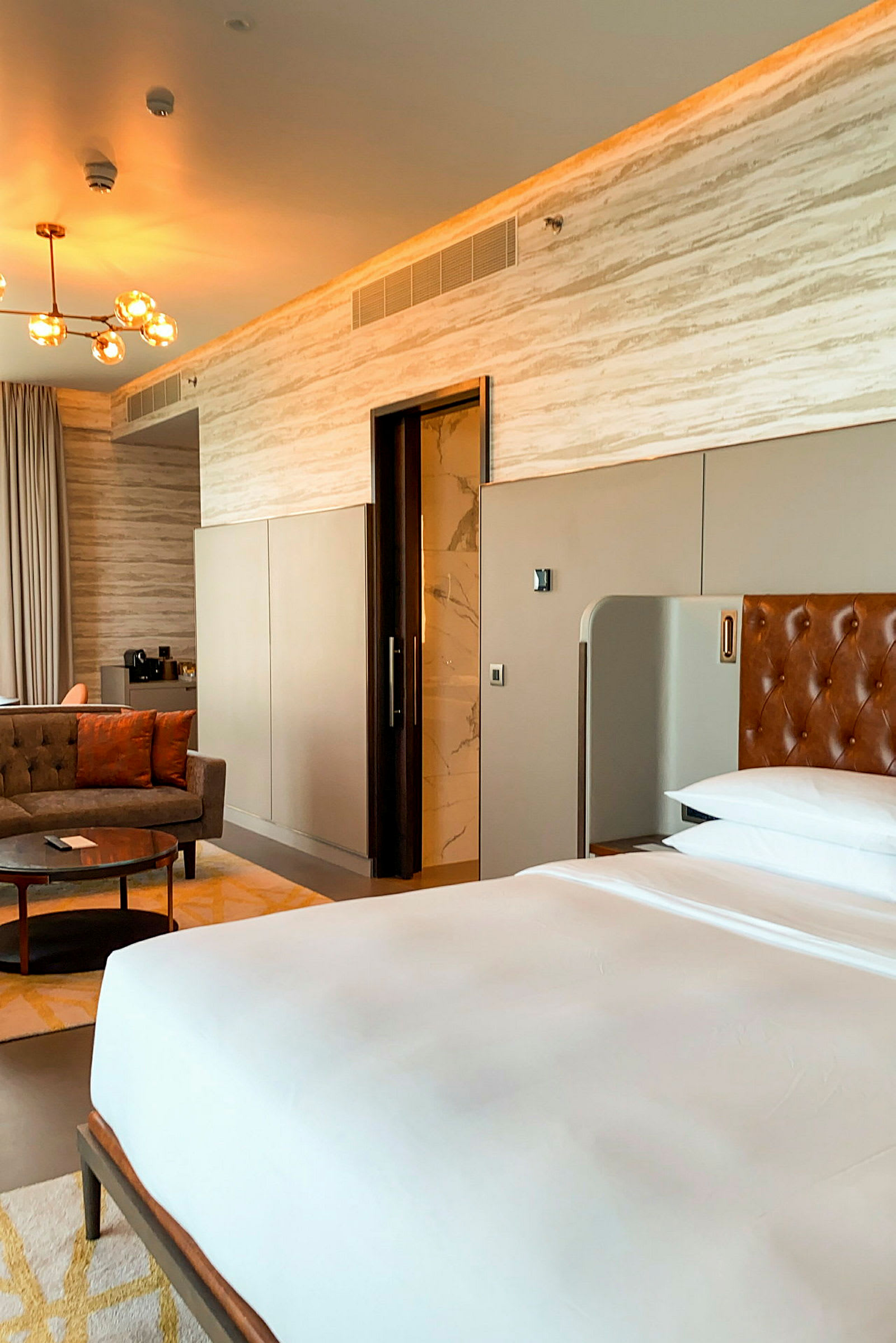 Moderni hotellihuone, jossa on sänky, istuinalue ja pääsy kylpyhuoneeseen. (Tekoälyn luoma teksti)