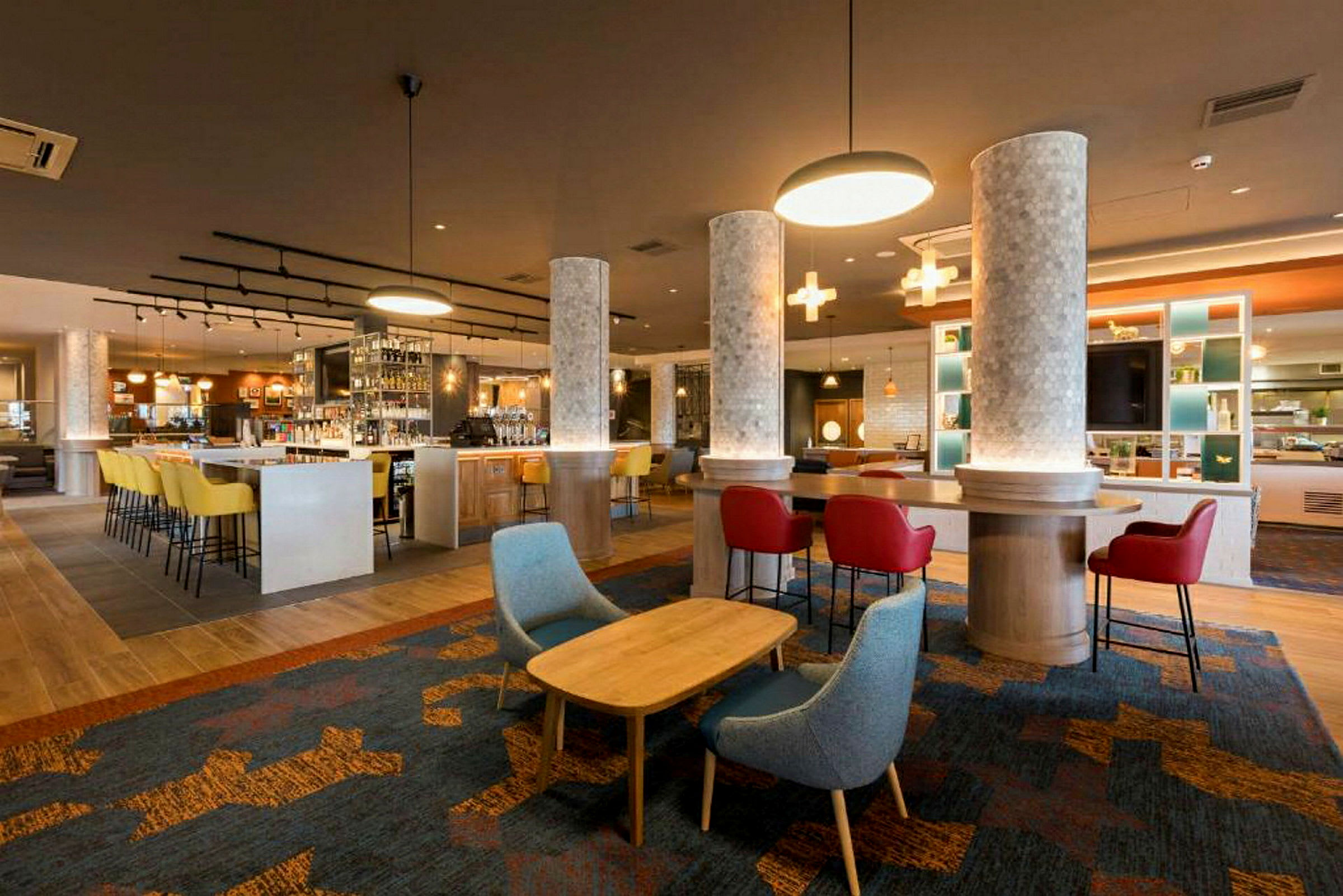 Moderni hotellibaari, jossa on värikkäitä tuoleja ja valaistus. (Tekoälyn luoma teksti)