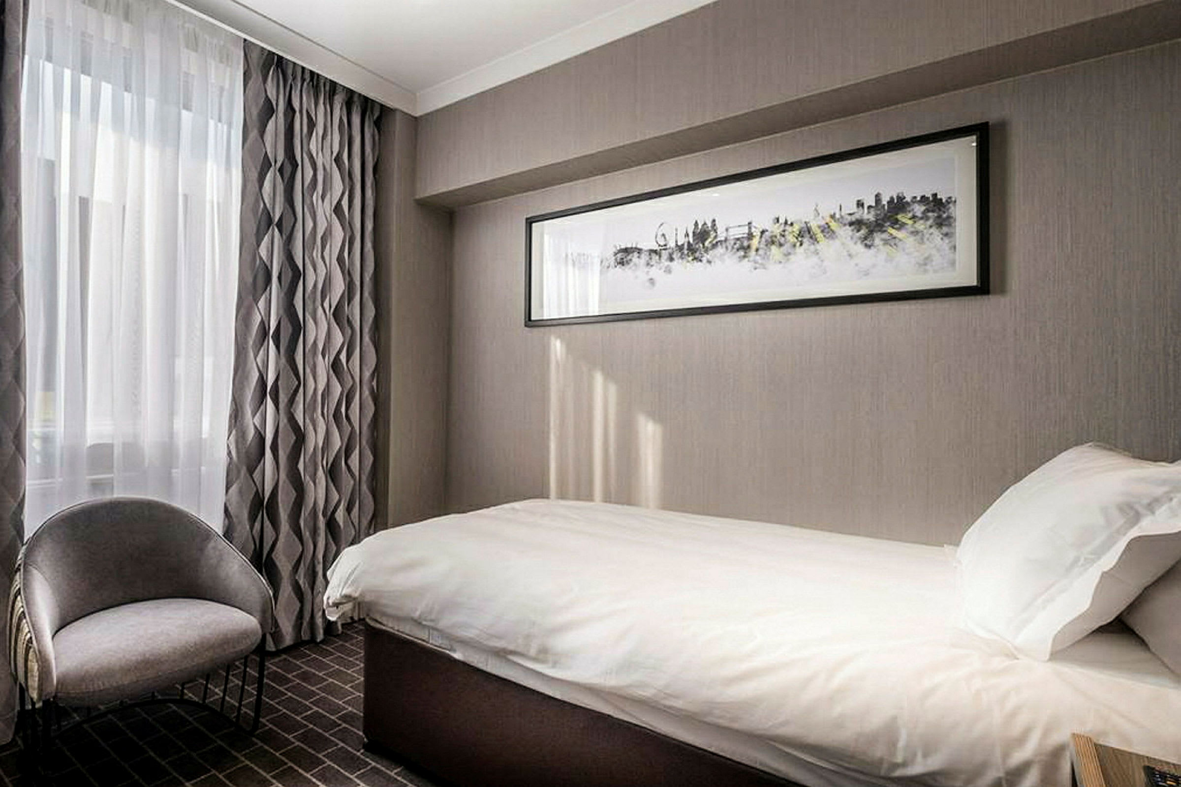Hotellihuone, jossa on yhden hengen sänky ja tuoli, koristeltu harmahtavilla sävyillä. (Tekoälyn luoma teksti)