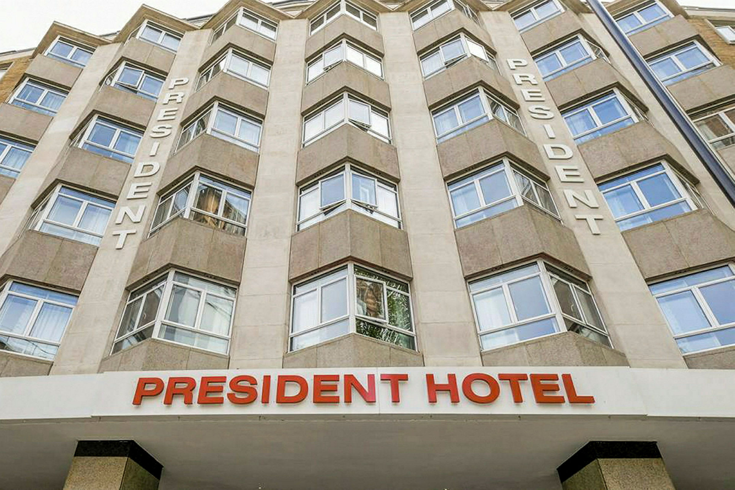President Hotelin klassinen julkisivu suurilla ikkunoilla ja tekstillä 'President' seinässä. (Tekoälyn luoma teksti)