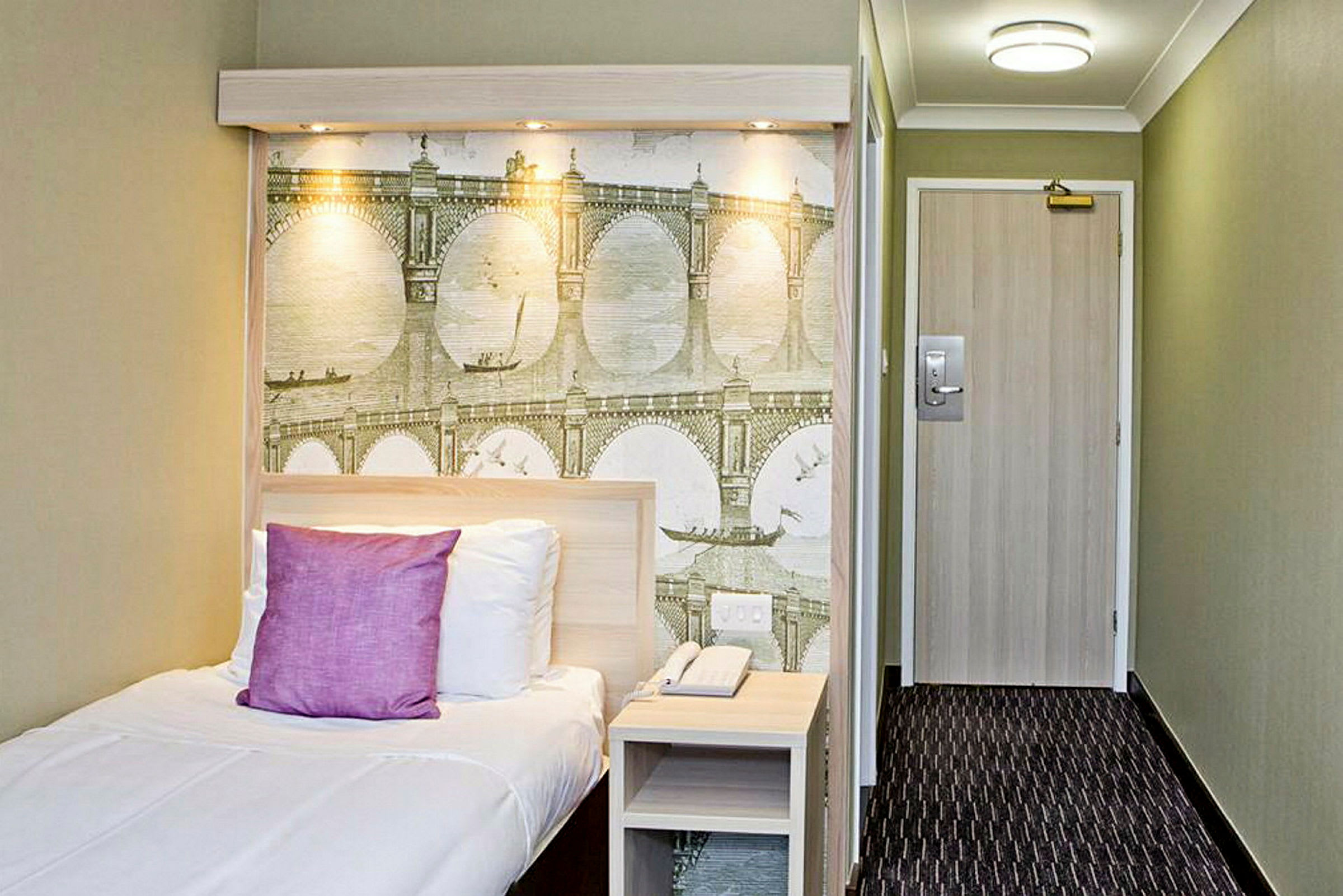Hotellihuone, jossa on yhden hengen vuode ja seinämaalaus silta-aiheella. (Tekoälyn luoma teksti)