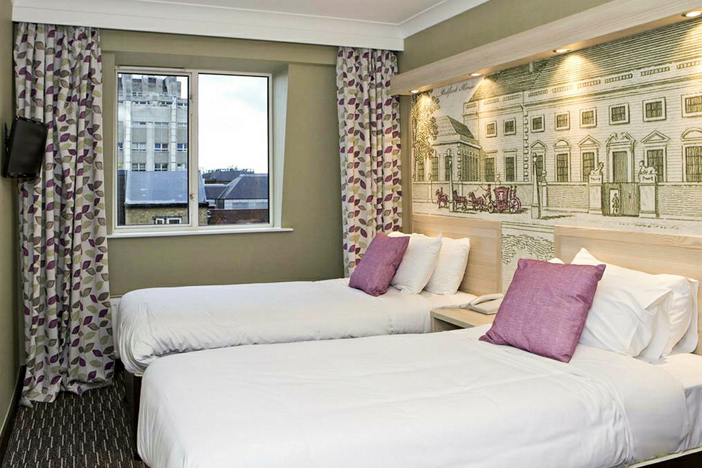 Hotellihuone, jossa on kaksi yhden hengen vuodetta ja koristeellinen seinä vuoteiden takana. (Tekoälyn luoma teksti)