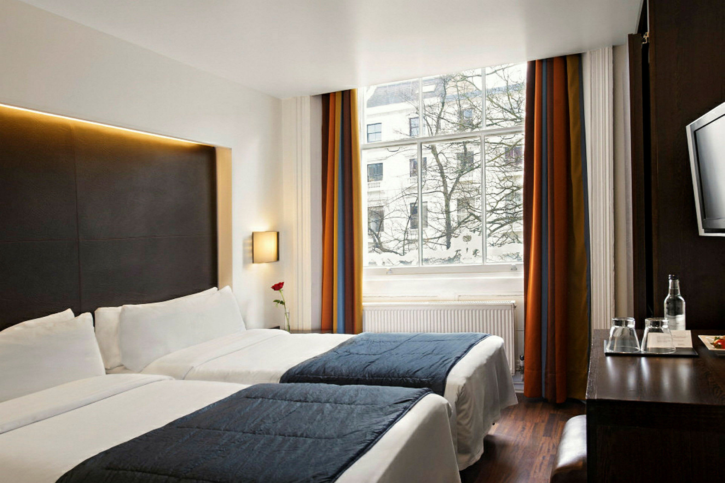 Hotellihuone, jossa kaksi yhden hengen sänkyä, suuret ikkunat ja näkymä lumisten puiden yli. (Tekoälyn luoma teksti)