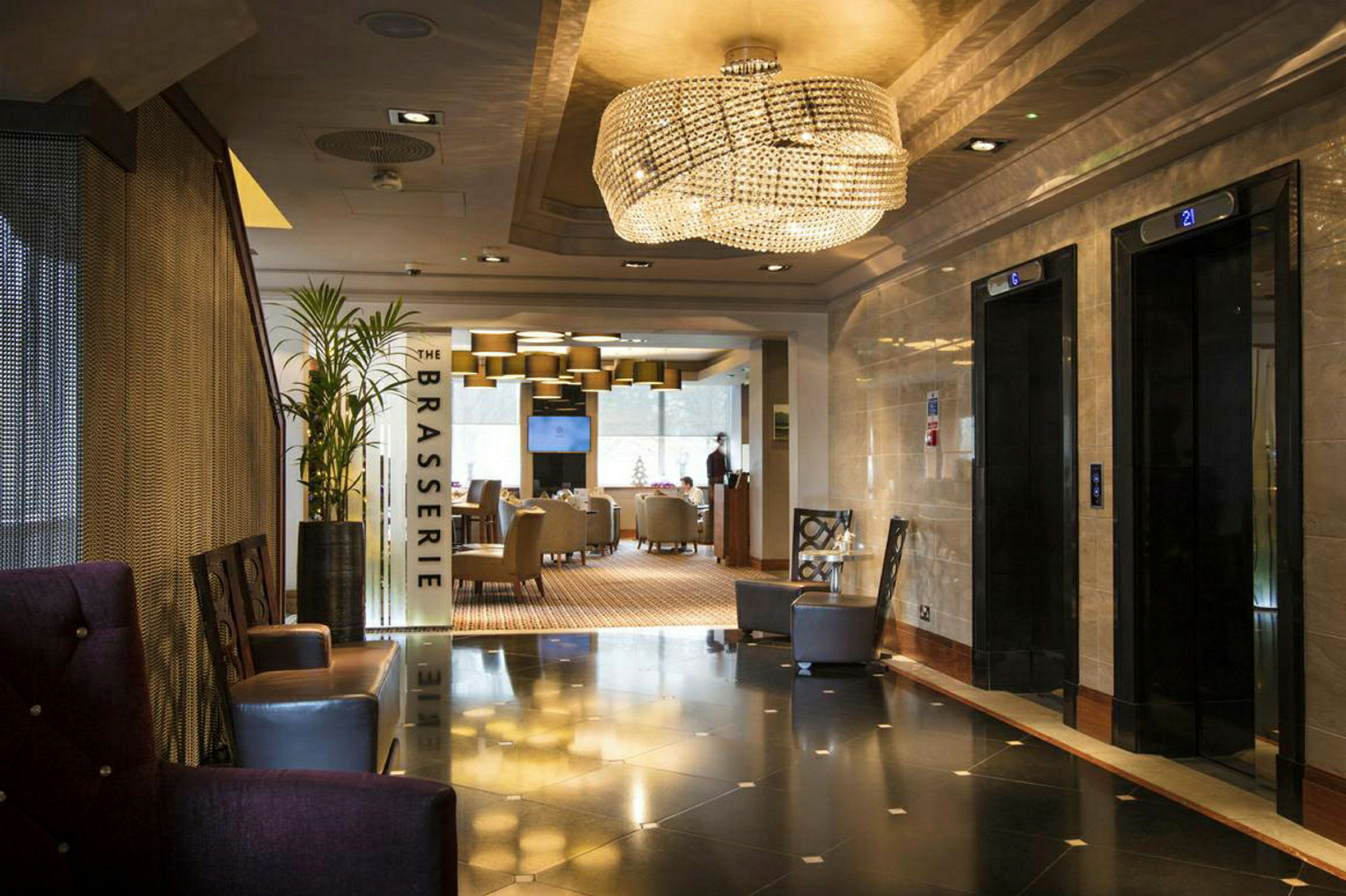 Hotellin aula, jossa hissit oikealla ja ravintolan 'The Brasserie' sisäänkäynti suoraan edessä. (Tekoälyn luoma teksti)