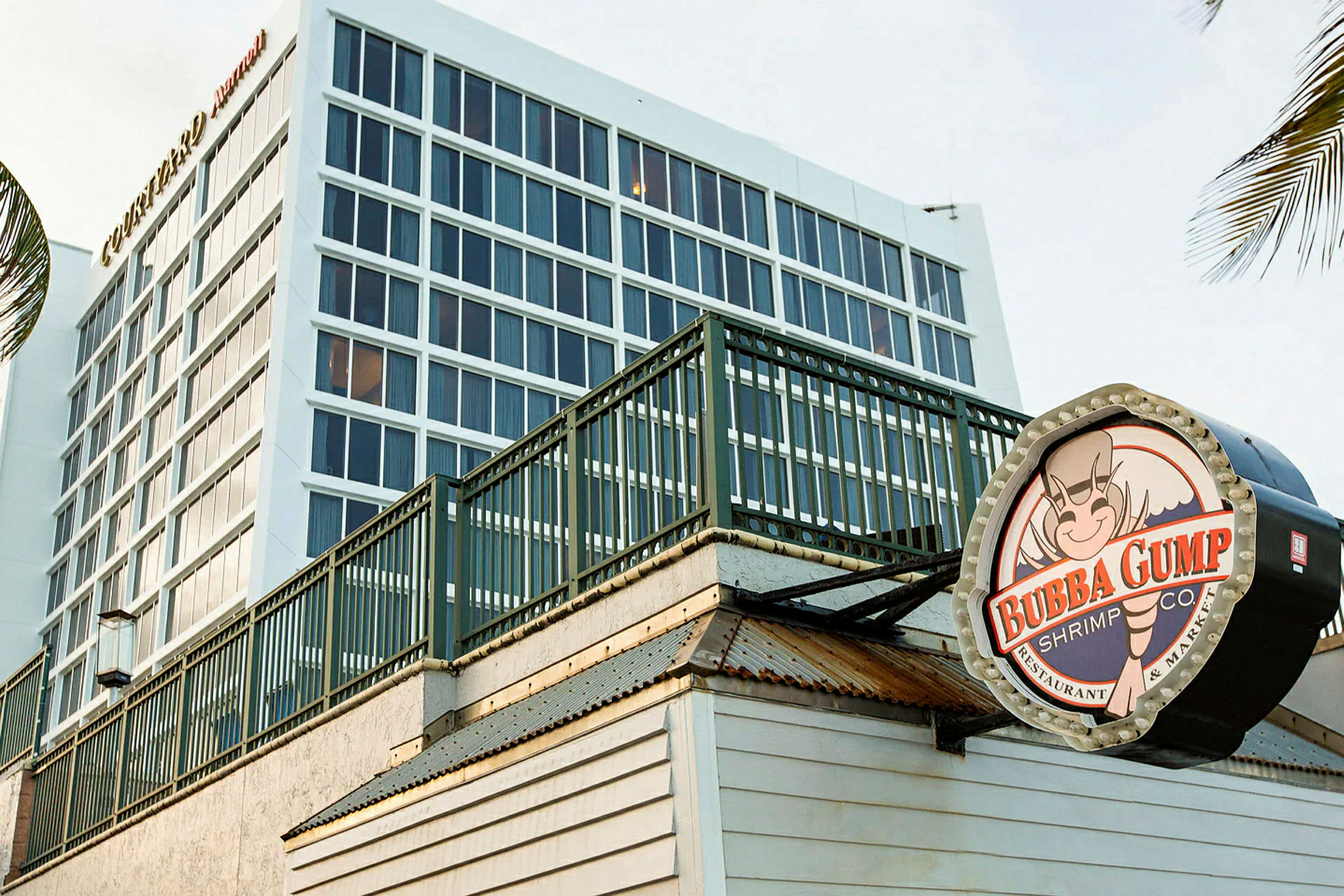 Taustalla nykyaikainen rakennus, jossa on suuret ikkunat, ja etualalla kyltti ravintolasta Bubba Gump Shrimp Co. (Tekoälyn luoma teksti)