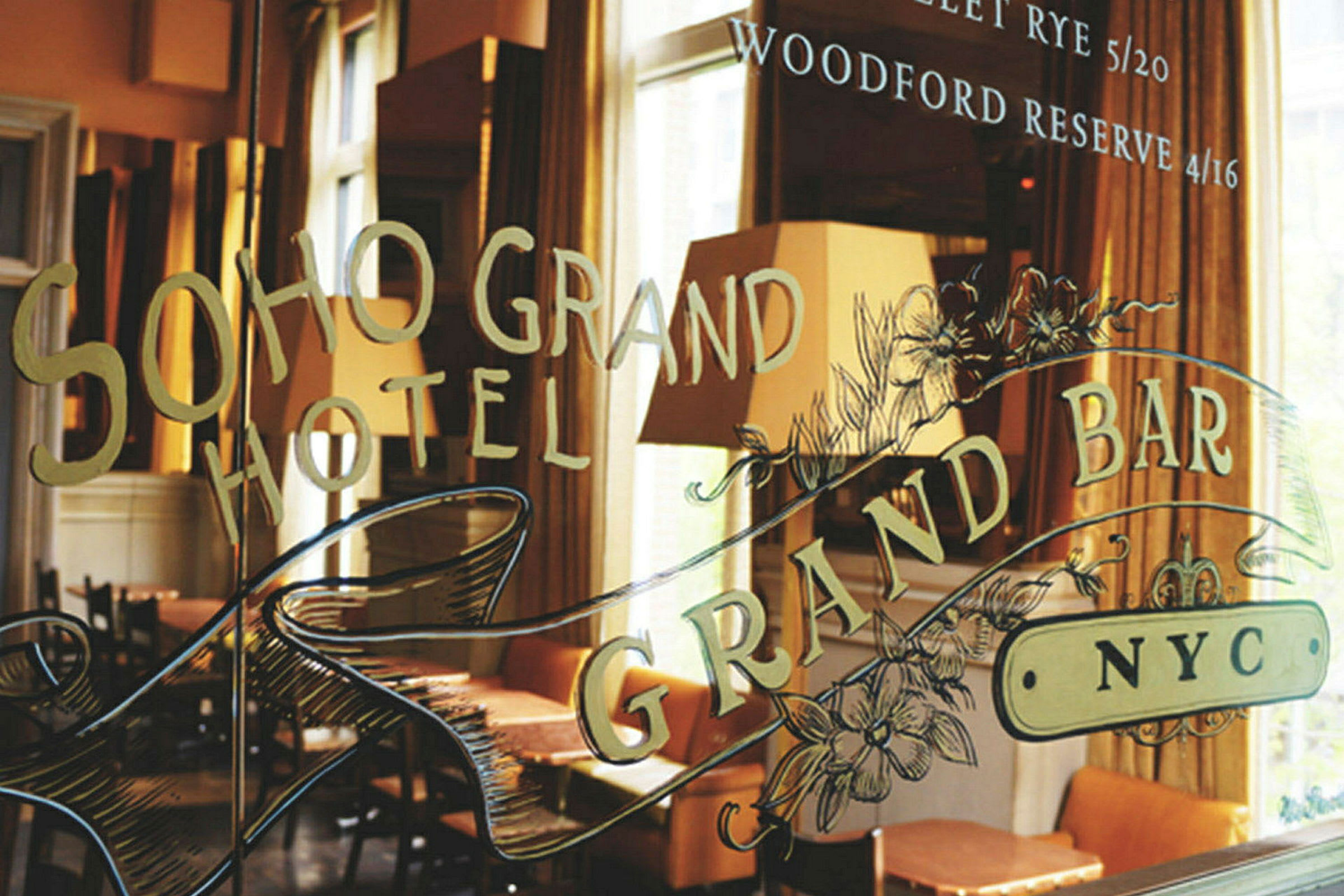 Ikkuna, jossa lukee 'Soho Grand Hotel' ja 'Grand Bar NYC,' sekä koristeluja. Taustalla näkyy huonekaluja ja lamppuja. (Tekoälyn luoma teksti)