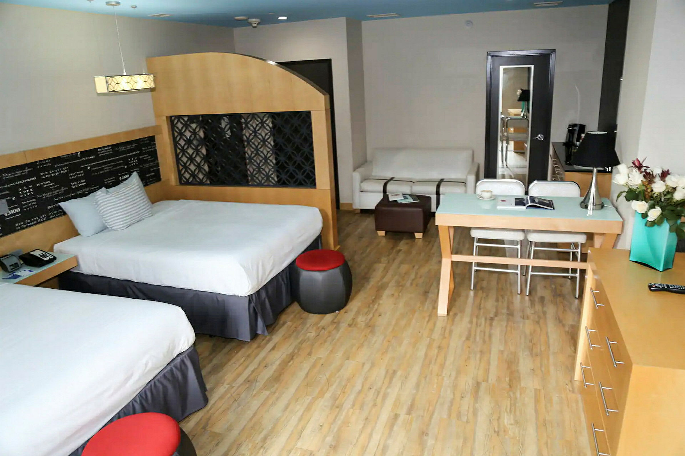 Hotellihuone, jossa on kaksi vuodetta, pöytä, sohva ja kaappi. (Tekoälyn luoma teksti)