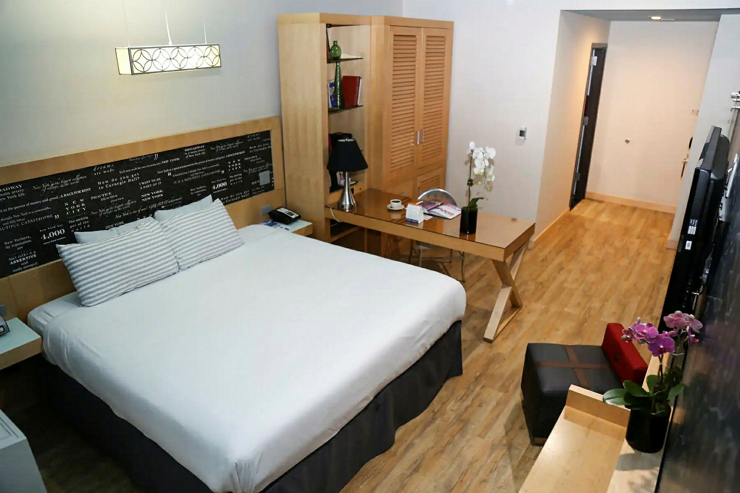 Hotellihuone, jossa on parivuode, kirjoituspöytä, kaappi ja tuoli, sisustettu pehmeillä väreillä ja moderneilla huonekaluilla. (Tekoälyn luoma teksti)