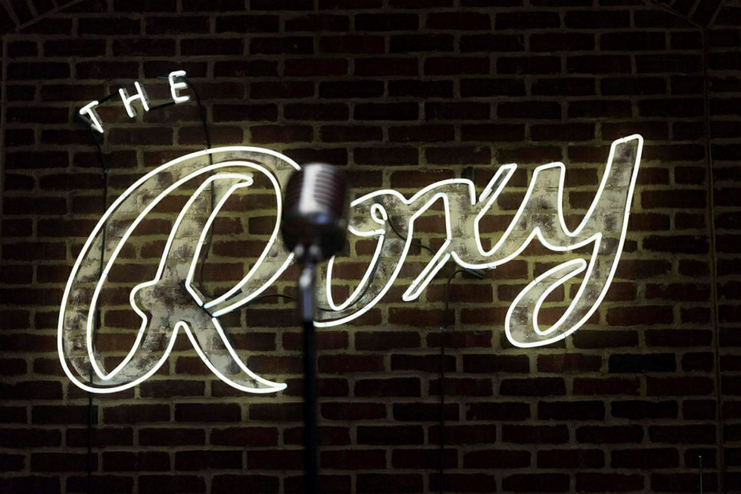 Mikrofoni neonkyltin edessä, jossa lukee "The Roxy", tiiliseinällä. (Tekoälyn luoma teksti)