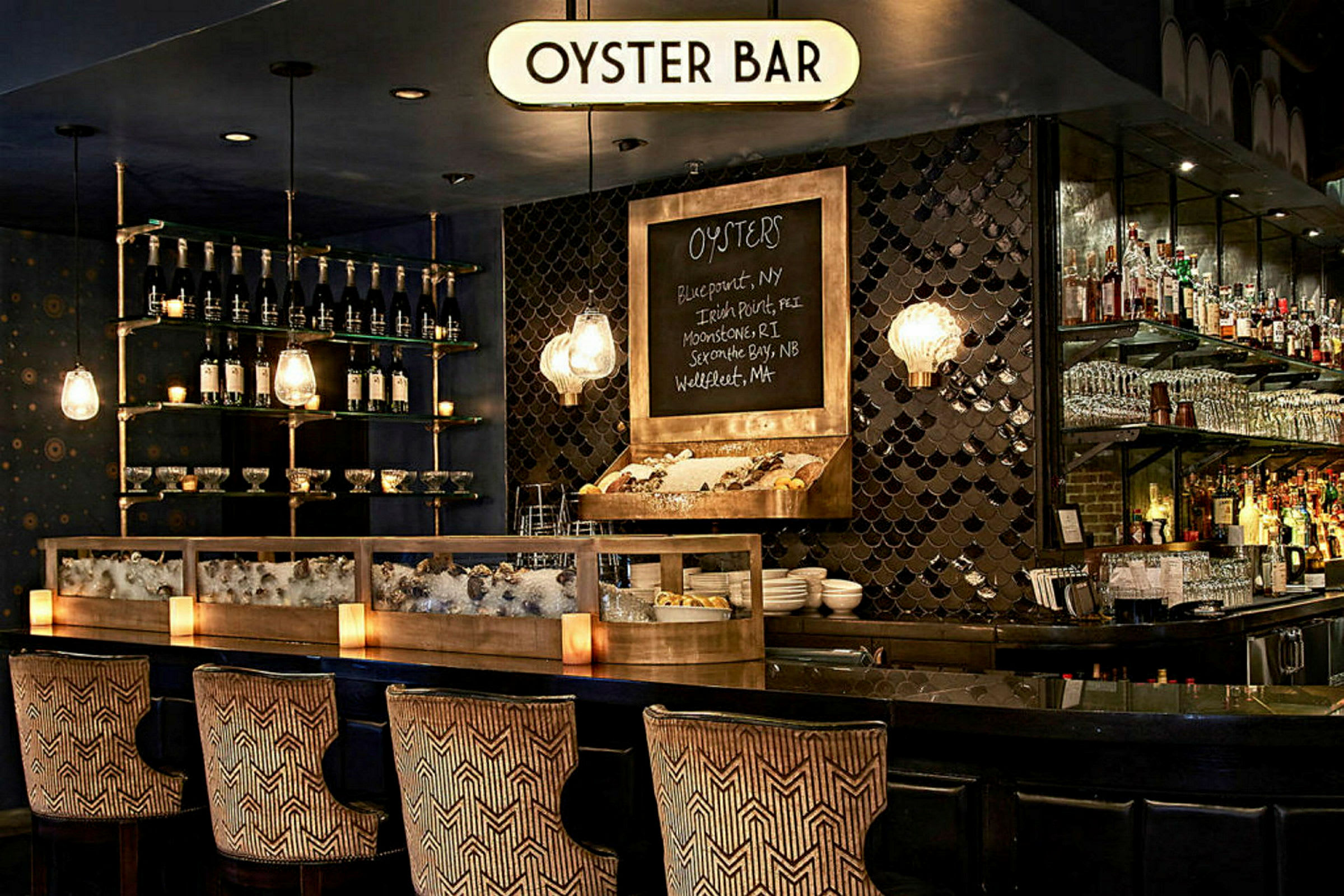 Tyylikäs osteribaari, jossa tiski täynnä jäätä ja ostereita, pulloja ja laseja hyllyillä sekä koristeellisia valaisimia. (Tekoälyn luoma teksti)