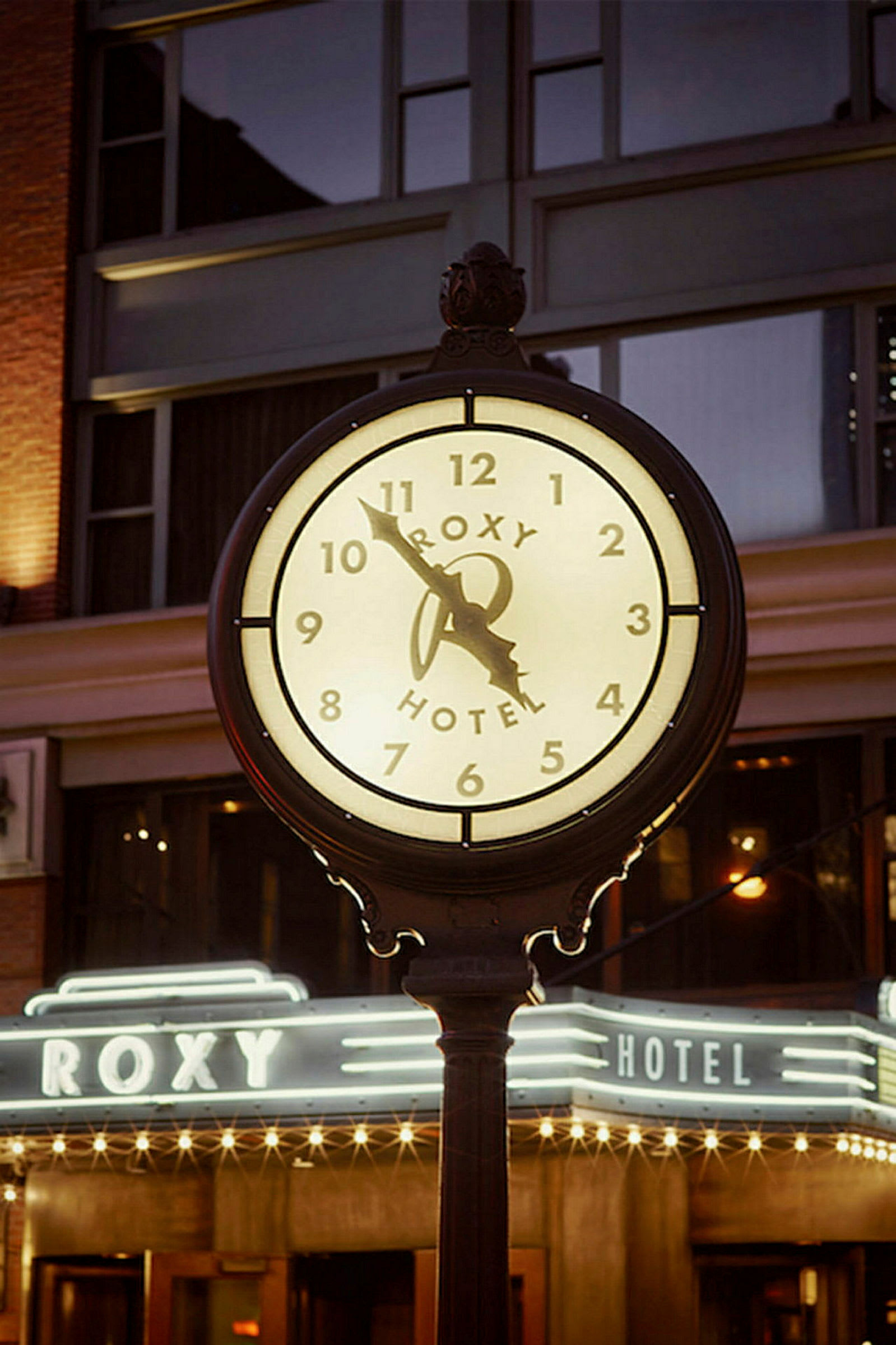 Valaiseva kello, jossa lukee "Roxy Hotel", sijaitsee rakennuksen edessä ilta-aikaan. (Tekoälyn luoma teksti)