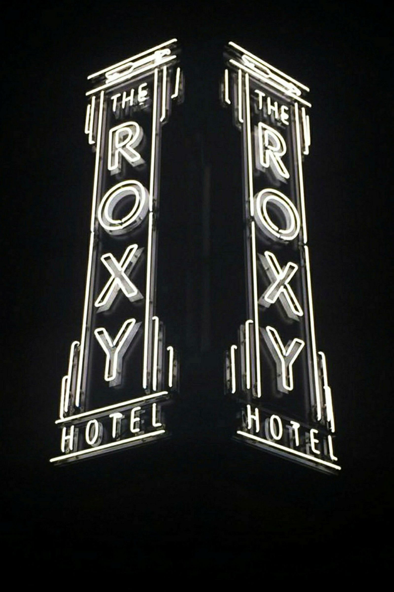 Neonvaloilla varustettu kyltti, jossa lukee "The Roxy Hotel" ja joka loistaa pimeydessä. (Tekoälyn luoma teksti)