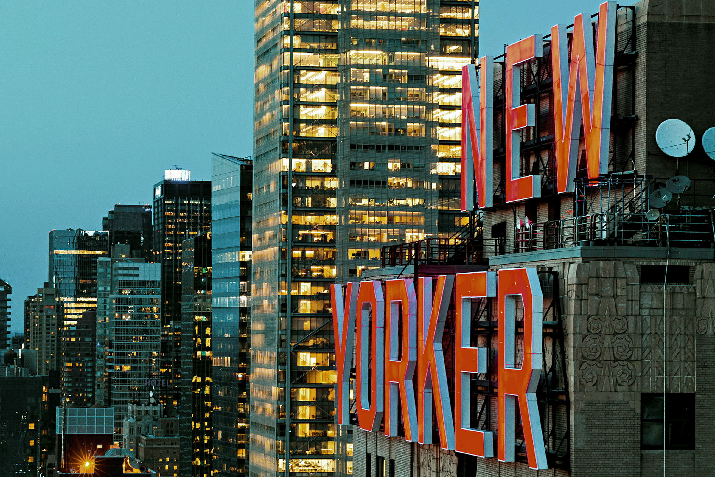 Kuva rakennuksesta, jossa on suuret punaiset kirjaimet "New Yorker", ja taustalla näkyy useita moderneja rakennuksia. (Tekoälyn luoma teksti)