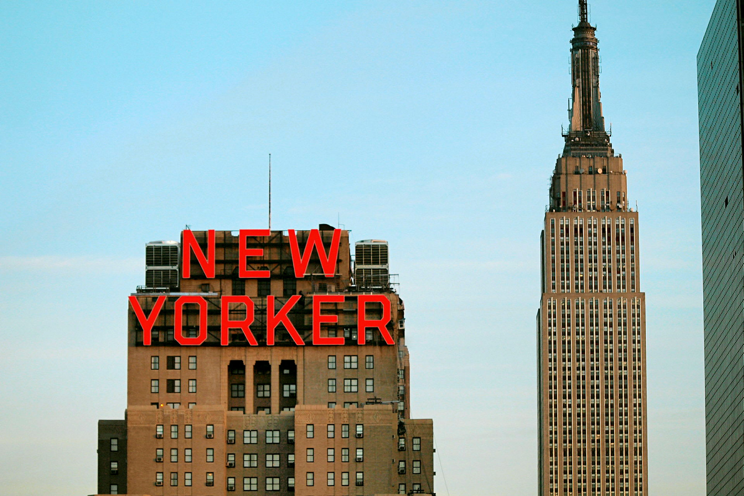 Kuva rakennuksesta, jossa näkyy "New Yorker" -kyltti, ja taustalla Empire State Building. (Tekoälyn luoma teksti)