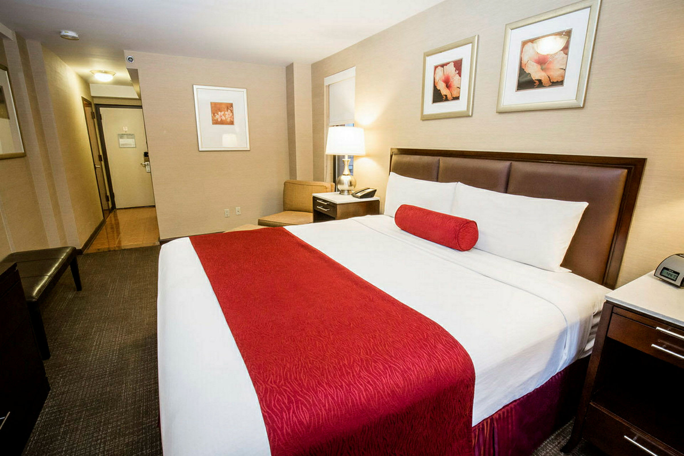 Hotellihuone, jossa suuri sänky punaisilla yksityiskohdilla. Kirjoituspöytä ja lampunvarjostin näkyvillä. (Tekoälyn luoma teksti)